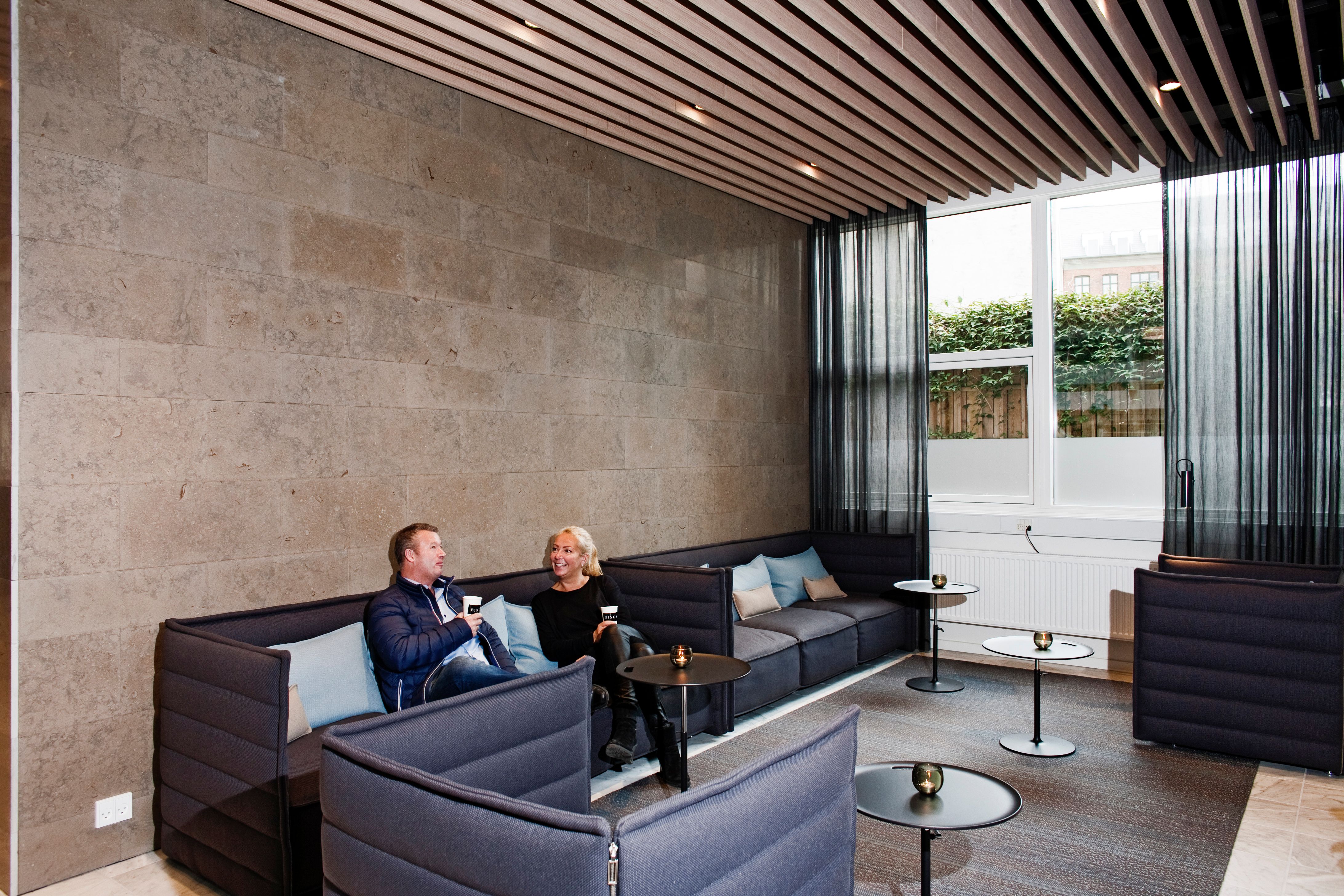 To personer nyder en kop varm drikke i en stor lounge i et kontorhus på Vesterbro med lyse og åbne vinduer
