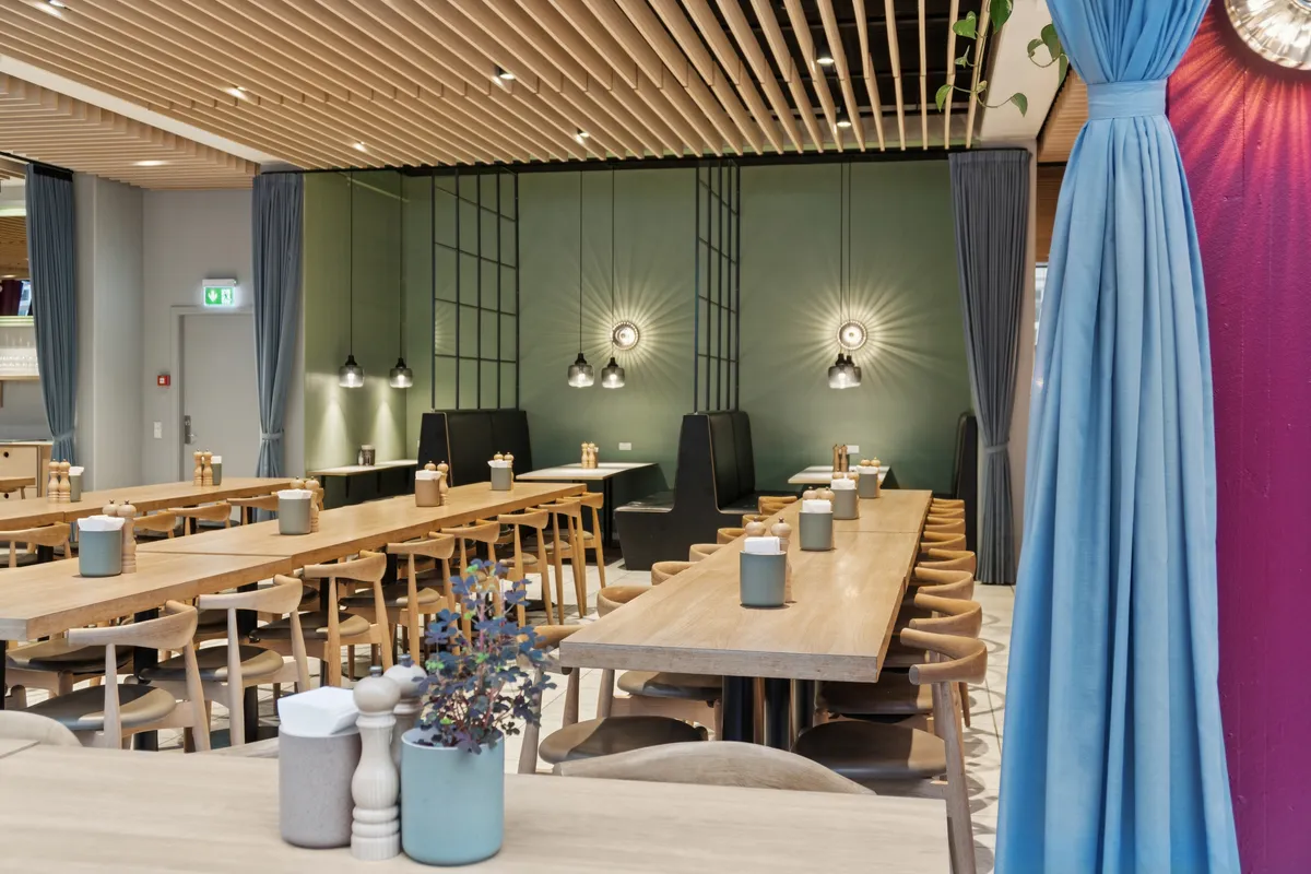 Lejet lokaler med lyse lofter og lysekroner i B!NGS kontorhus på Vesterbro. Bord med salt og peber samt en plante i vase i forgrunden. Bord og stole i baggrunden.