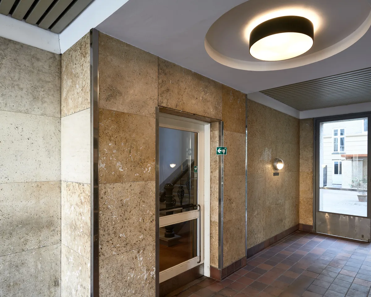 En nyrenoveret kontorgang med marmorvægge og lysekroner i loftet samt en glasdør og en trappe i baggrunden