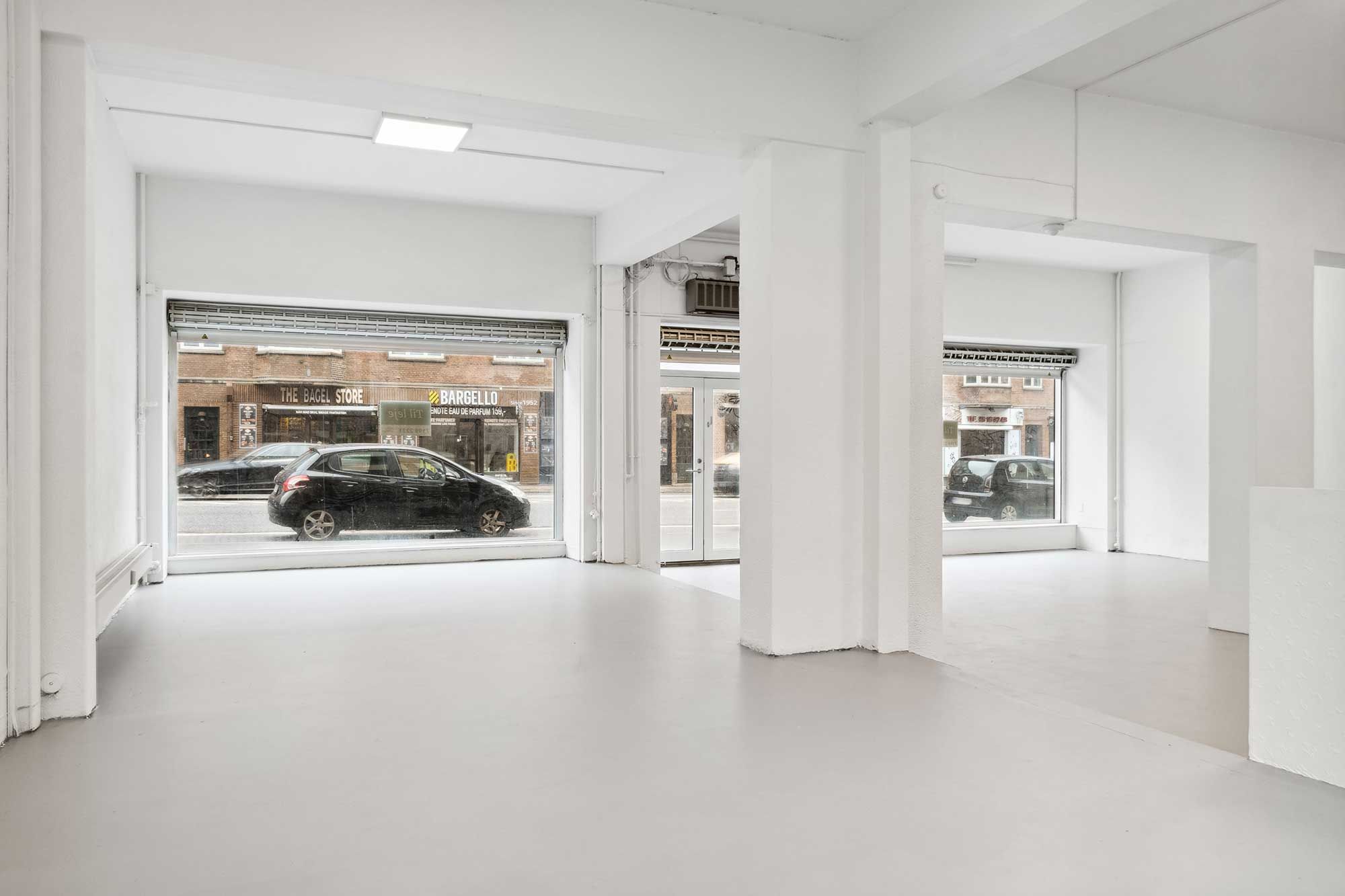 Hvidt lokale med store ruder og biler udenfor. En af butikkerne er The Bagel Store og et gulv med hvid maling