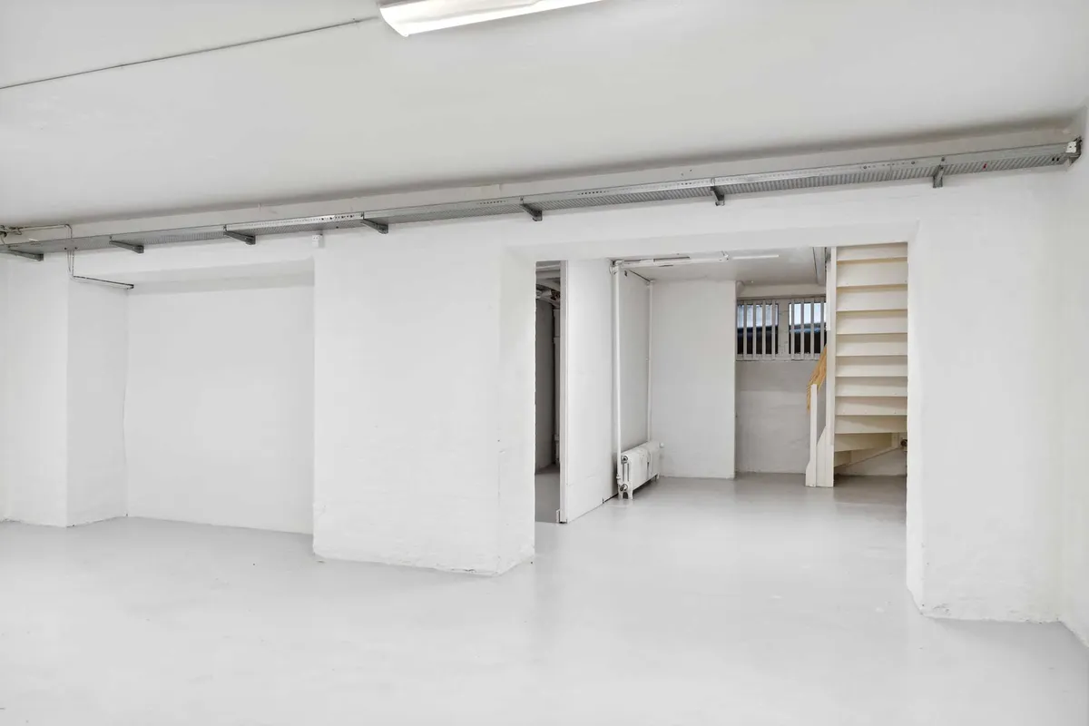 Et stort, ubenyttet lagerrum med hvide vægge og gulv samt en høj trappe og et radiatorpanel