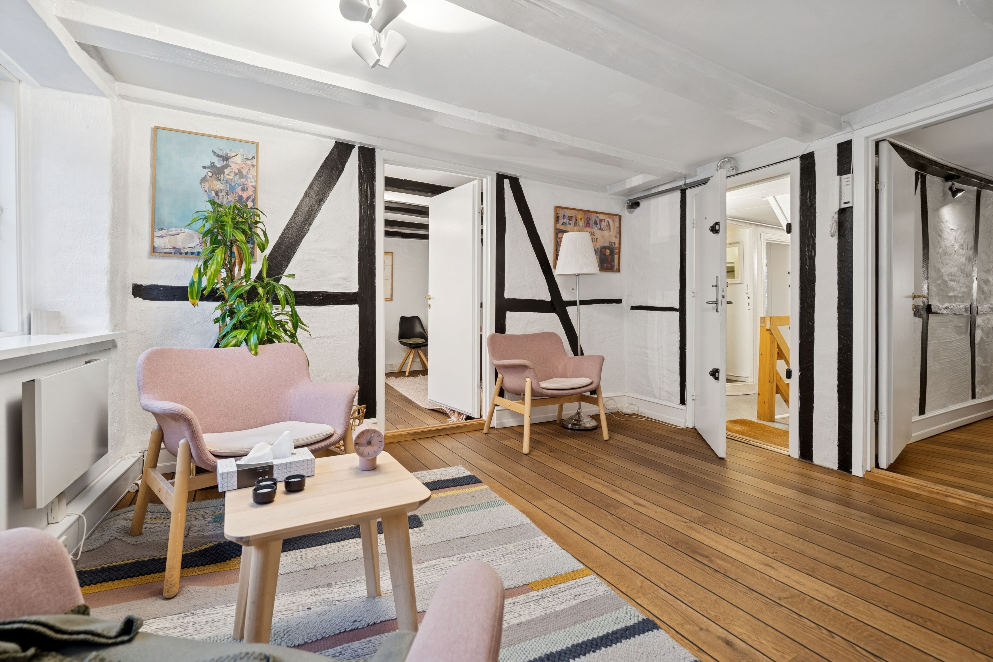 Lyst og funktionelt kontor med puder og plante, massivt trægulv og hvide vægge med sømløse mønstre