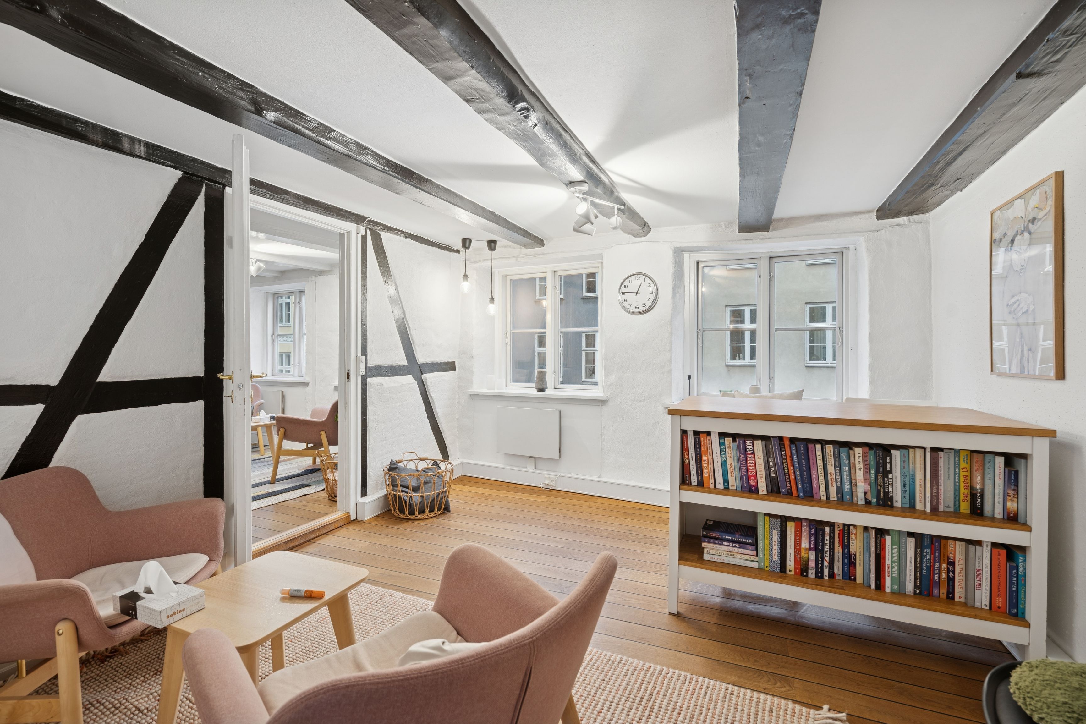 Funktionelt og lyse kontor med lyse trægulve og højloft. Indeholder møbler, et bibliotek, og en sofa. Adgang til bagvedliggende terrasse.