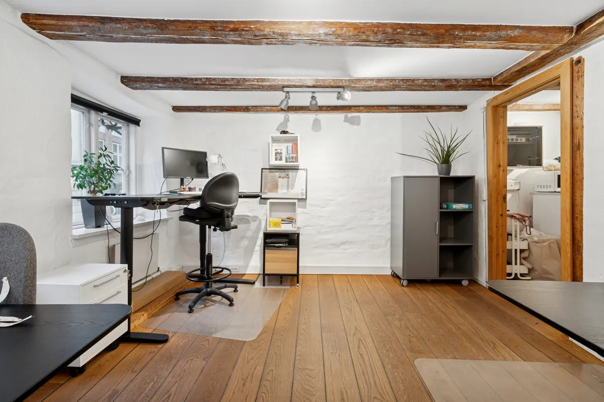 Lyst kontor med skrånende loft, højt gulv og store vinduer til Nørreport og byens liv. Komplet med moderne skrivebord, plante og bekvemme møbler.