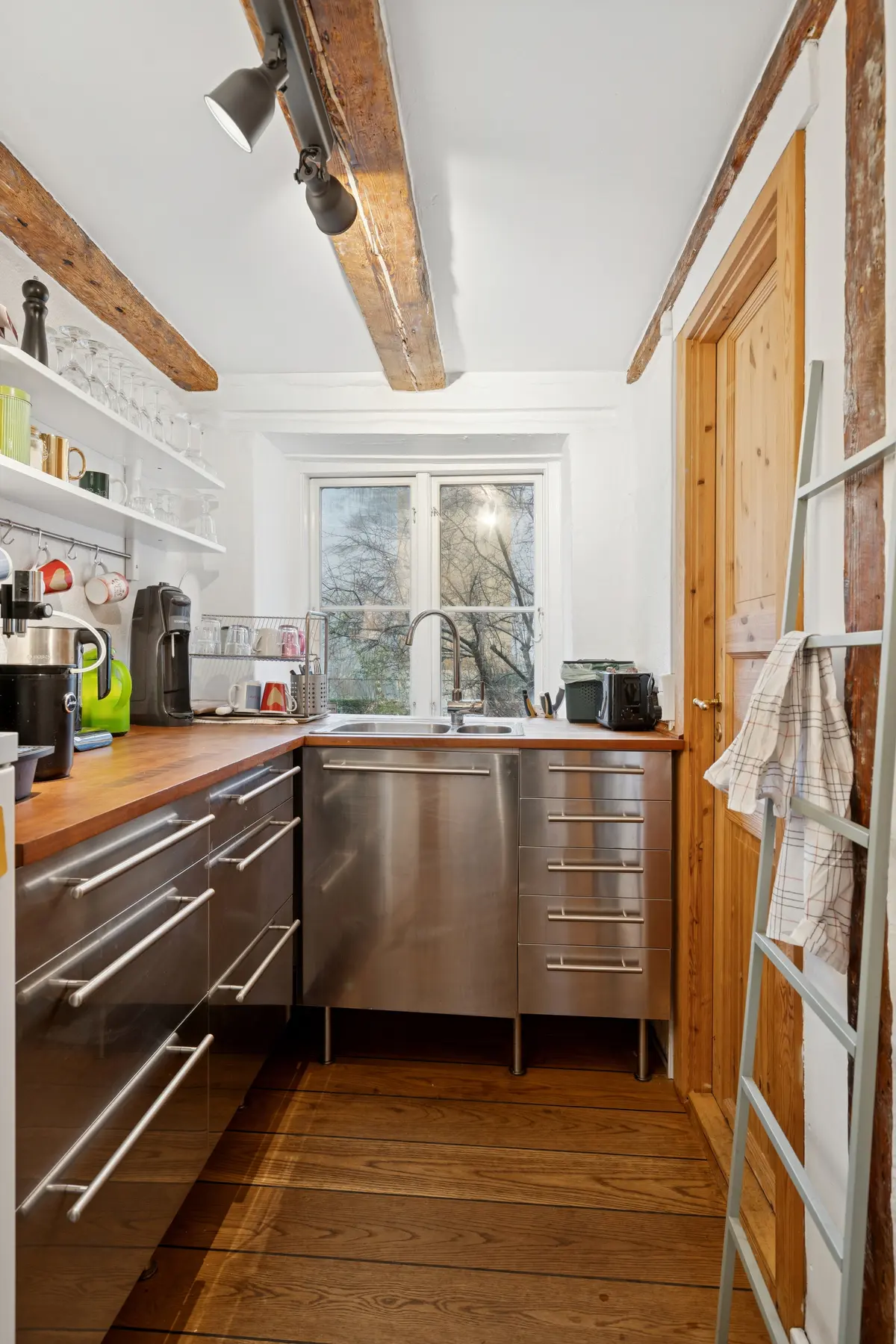 Rent og moderne køkken med højloft og åbent køkken, hvid væg, trægulv, rustfrit stålkøkken, trædør og trælejestykke med hængende tøj