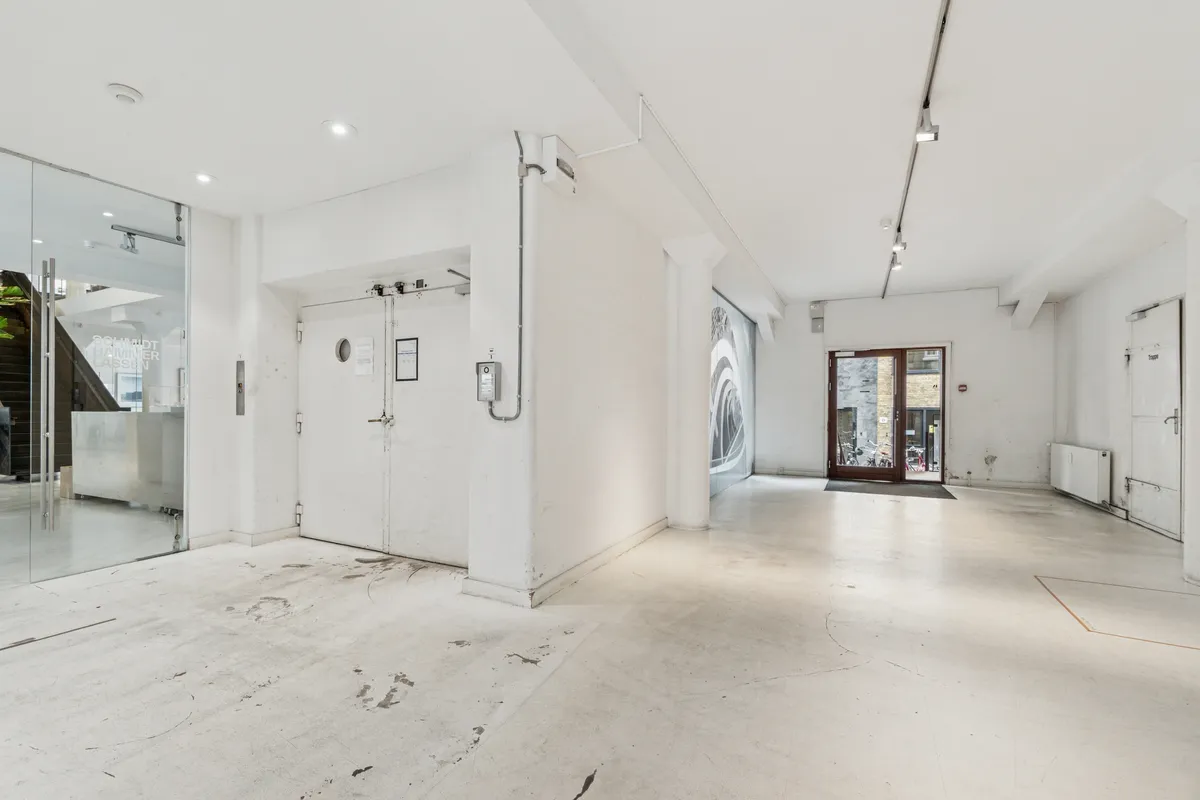 Lukket kontordør og glasdør med indgang og trappe. Hvid væg og gulv samt moderne belysning og vinduesparti. Møbler og tekstiler mangler endnu.