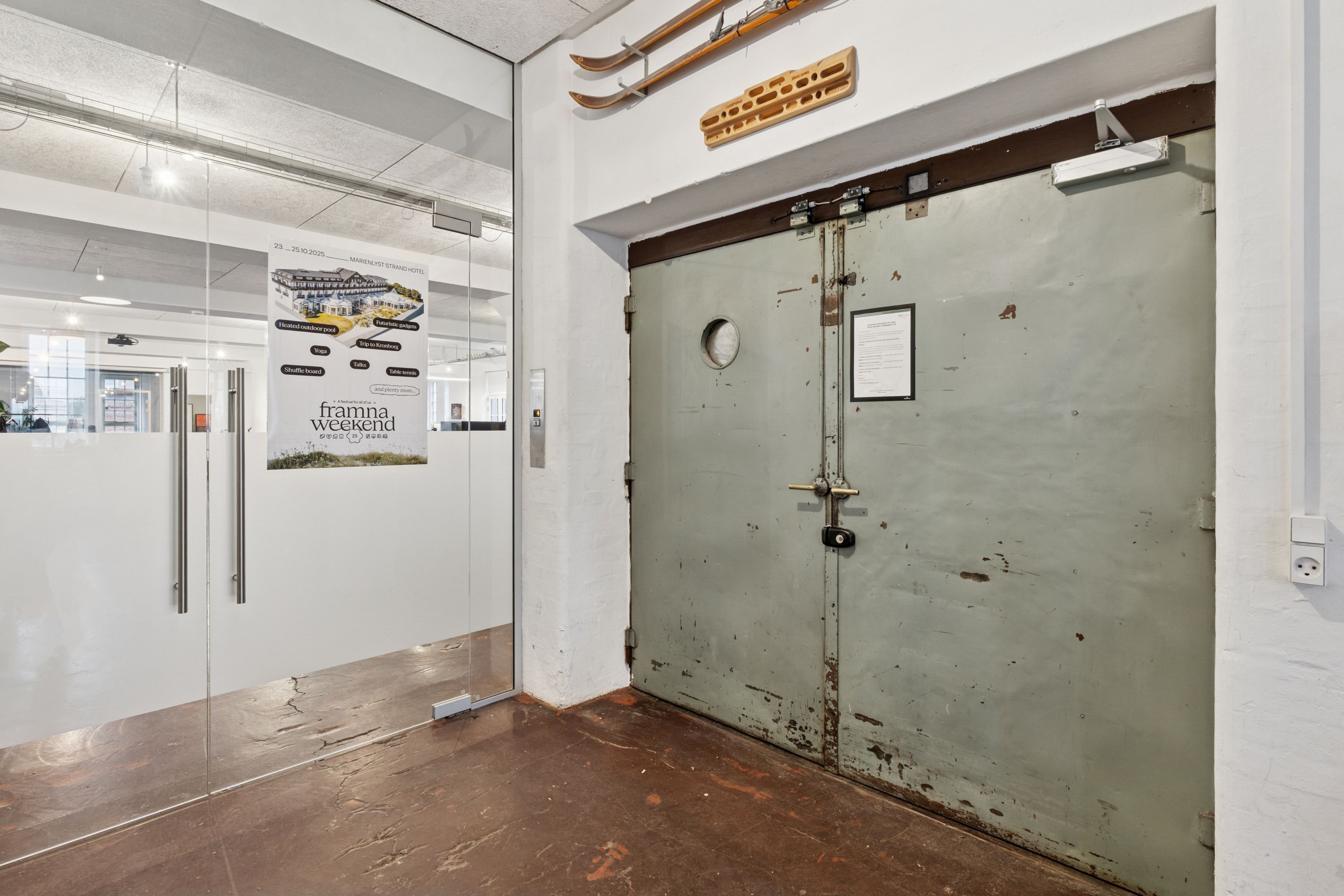 Kontor i gamle industribygning med store glasruder og lyse lofter, skihylde med gamle ski og dør med skjold og nummerplade