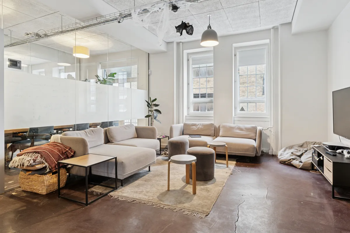 Kontorlokaler med lyse vinduer og lysekroner, skriveborde, sofaer, en stor tv og et skrivebord i en kontorlokalens loftsrum med et skrivebord og en plante