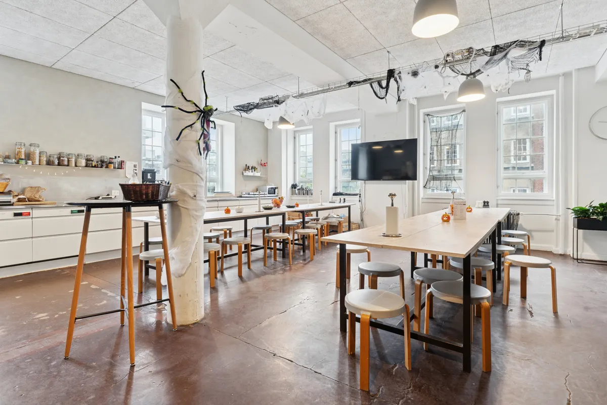 Kontor med møbler, højtloft, loftslampe, gulvbelægning og vinduer på Islands Brygge. Væg med hylder og små kurve og en stor spider.