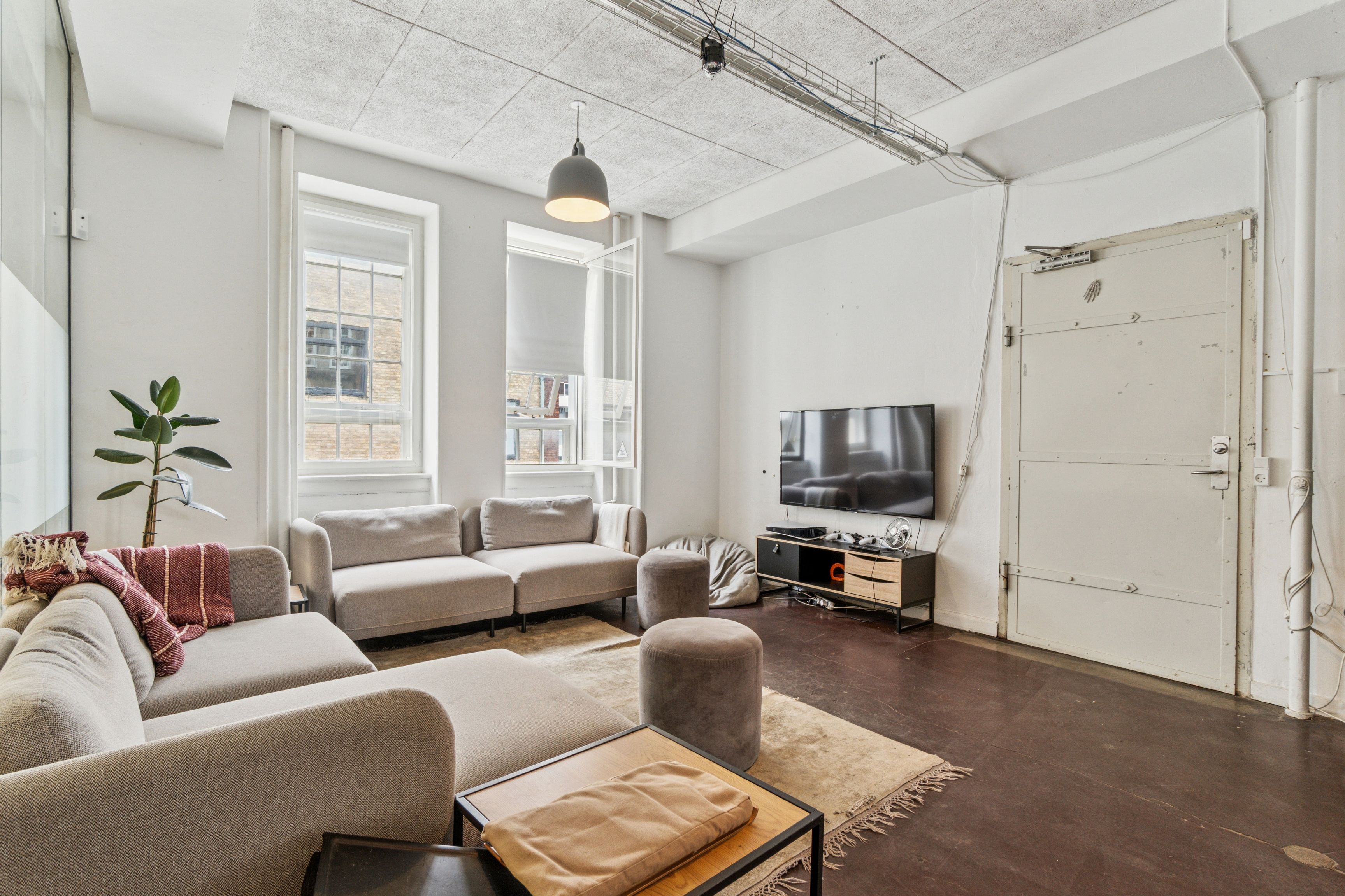 Kontorlokaler med moderne indretning og møbler, to sovesofaer og lyse vinduer, stort tv og plante ved væggen, tæt ved metrostation på Njalsgade 17A, København S