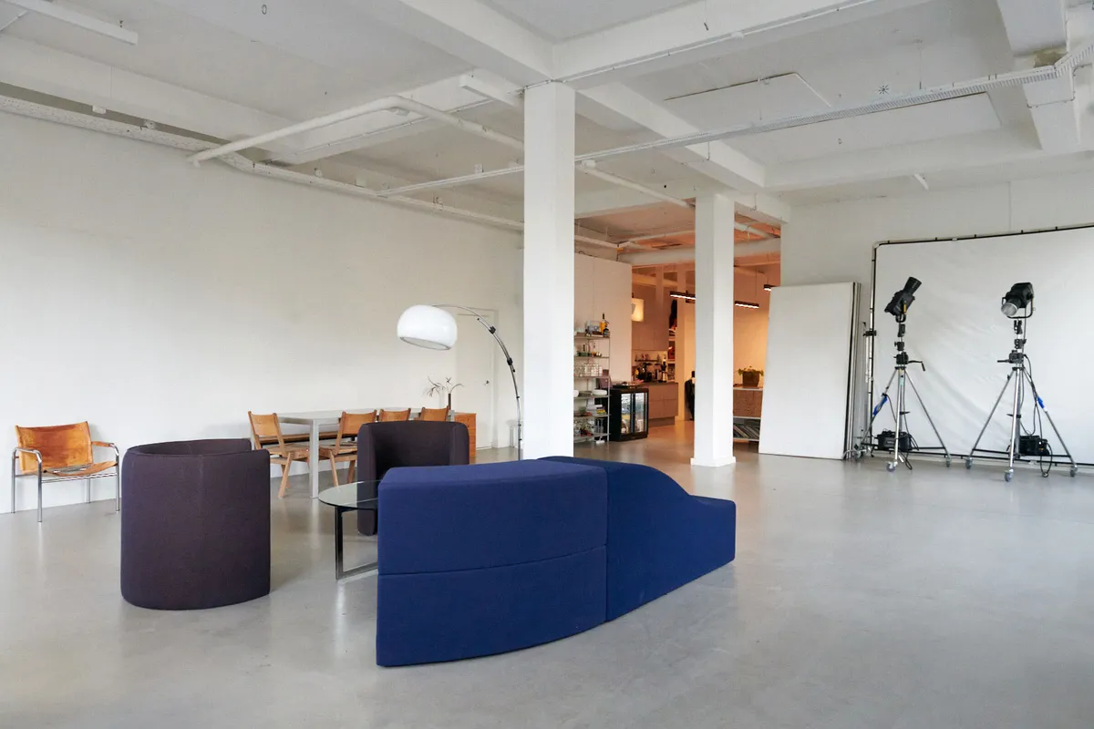 Kontor med store lyse vinduer og moderne møbler og en stor hvid væg, to stativer og kameraer samt en lysekronen og en stol i en skandinavisk stil