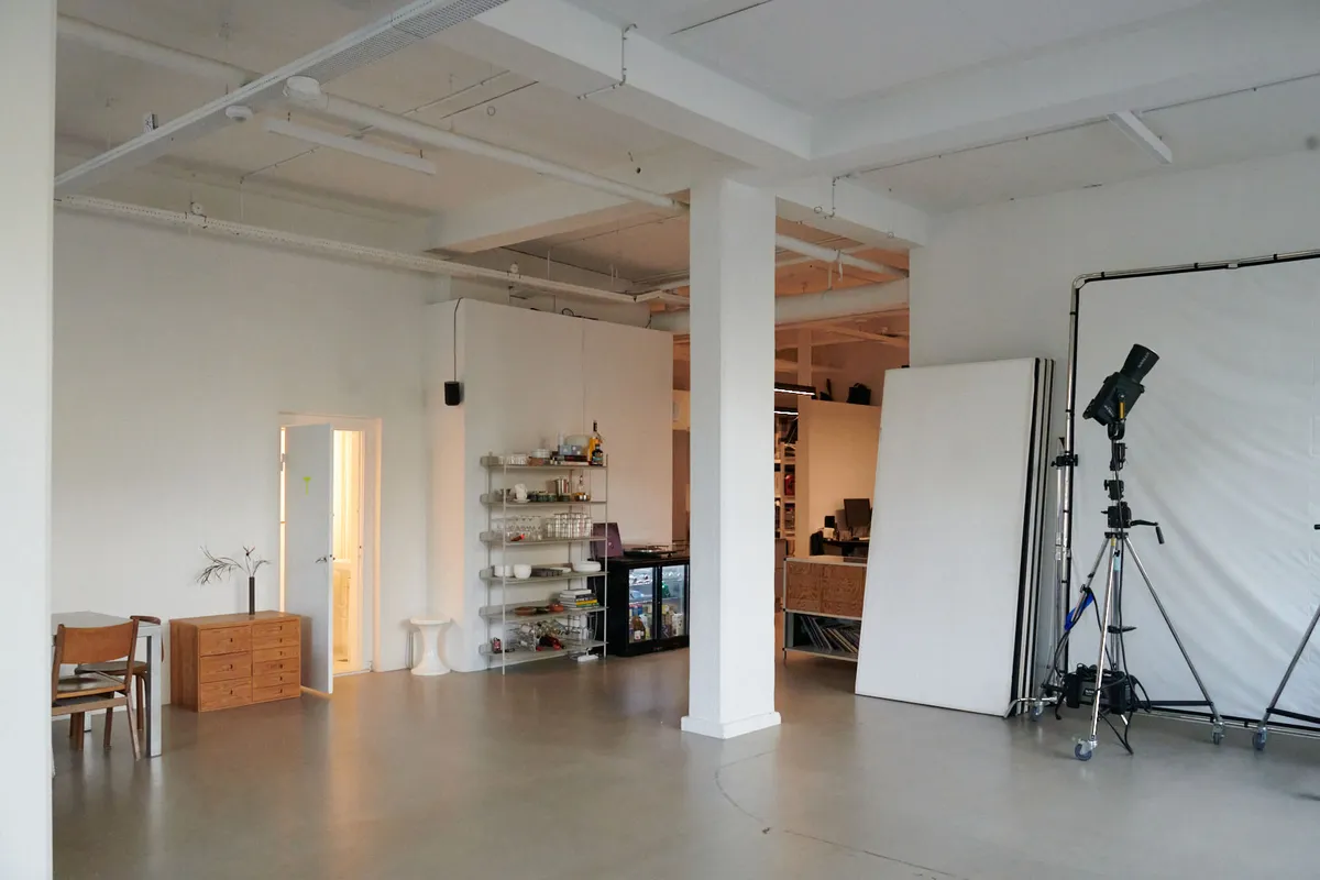 Kontorlokation i Nordvest med grønne områder og offentlig transport i nærheden. Indeholder en stor hvid væg og to høje kolonner samt et stativ med kamera.