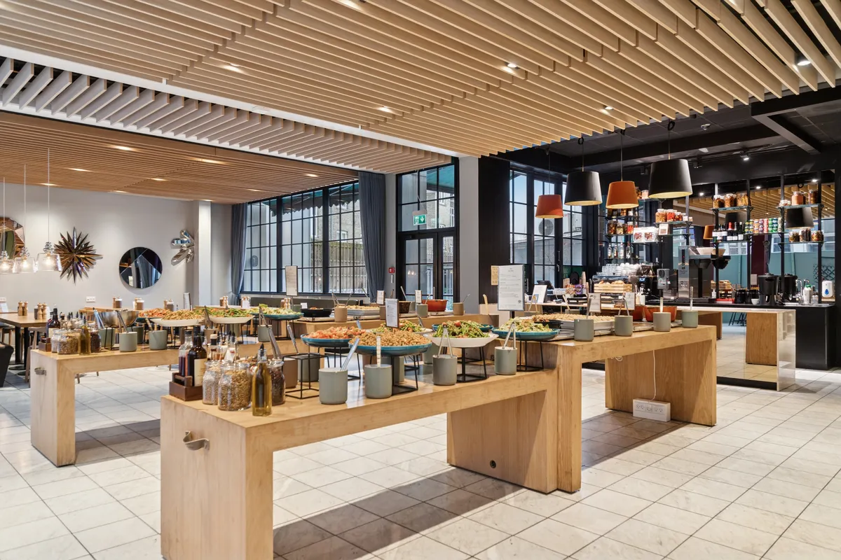 Kontorlokaler med moderne interiør, ventilation, træborde og lyse loftsbælte. En åben køkkendel med krydderier, grøntsager og drikkevarer. Lyskryds og store vinduer med udsigt til gaden.