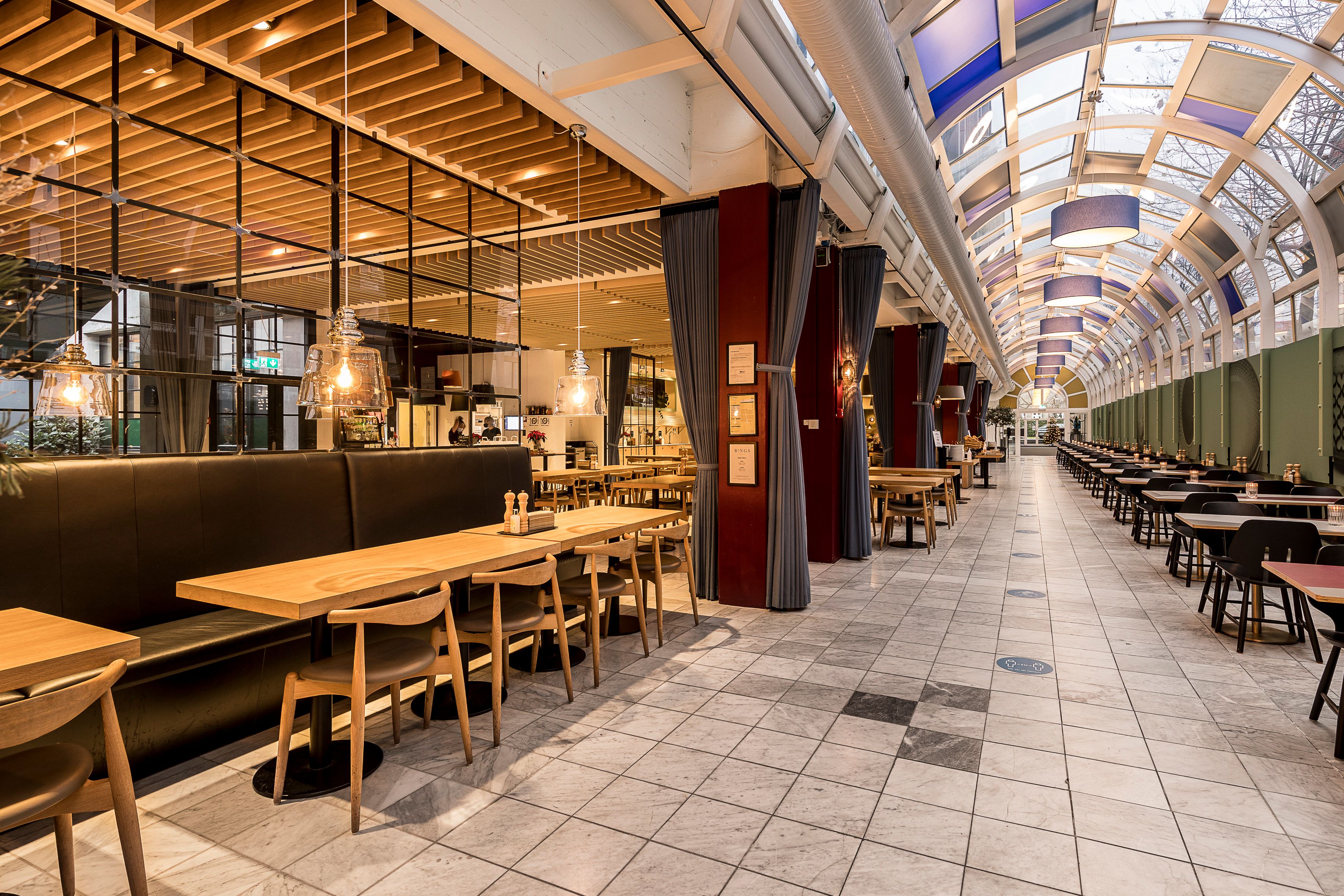 Moderne kontorrestaurant med lyse lofter og lysekroner, høje glasvægge og lyserøde søjler. Sorte og brunlæderede sofaer med lyse bænke. Marmorgulve og lyserøde søjler med møbler