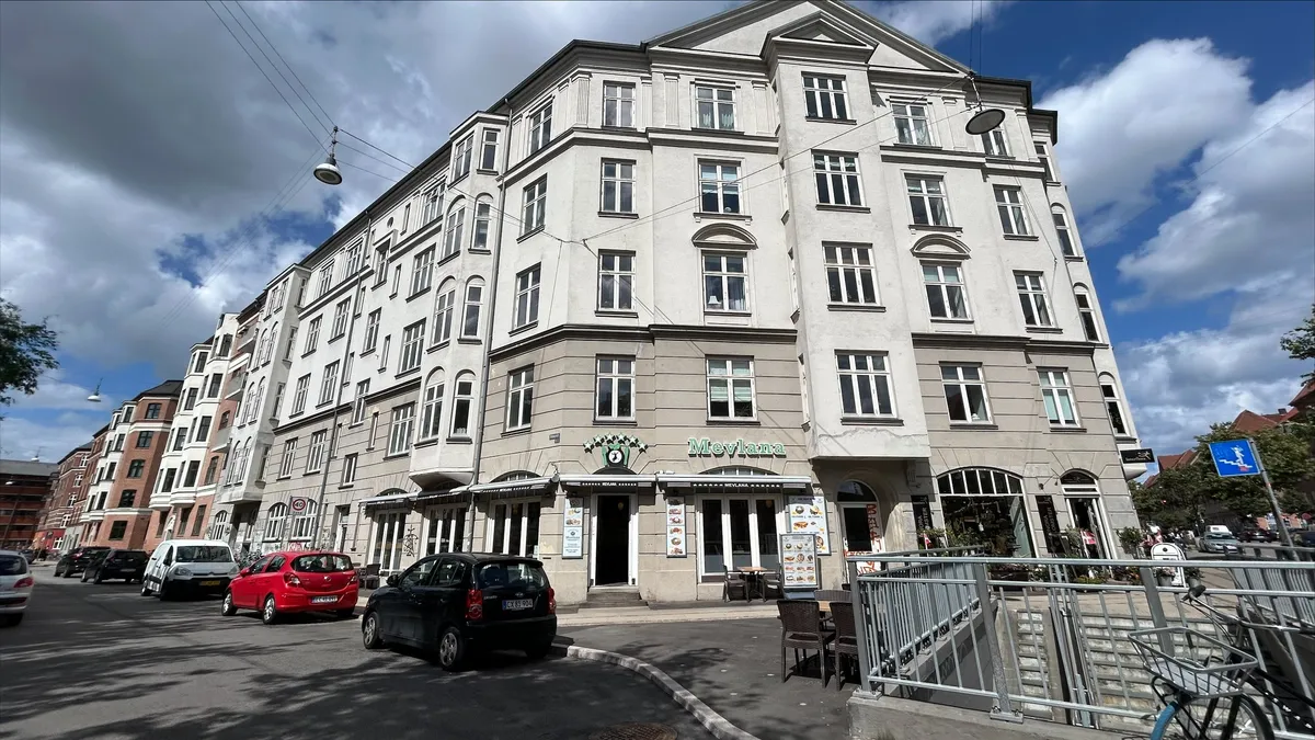 Restaurant Mevlana placeret på Jagtvej 119, København. Parkerede biler og cykler foran bygningen, sammen med gågade og skraldkurve. Tegn og reklame på facaden.