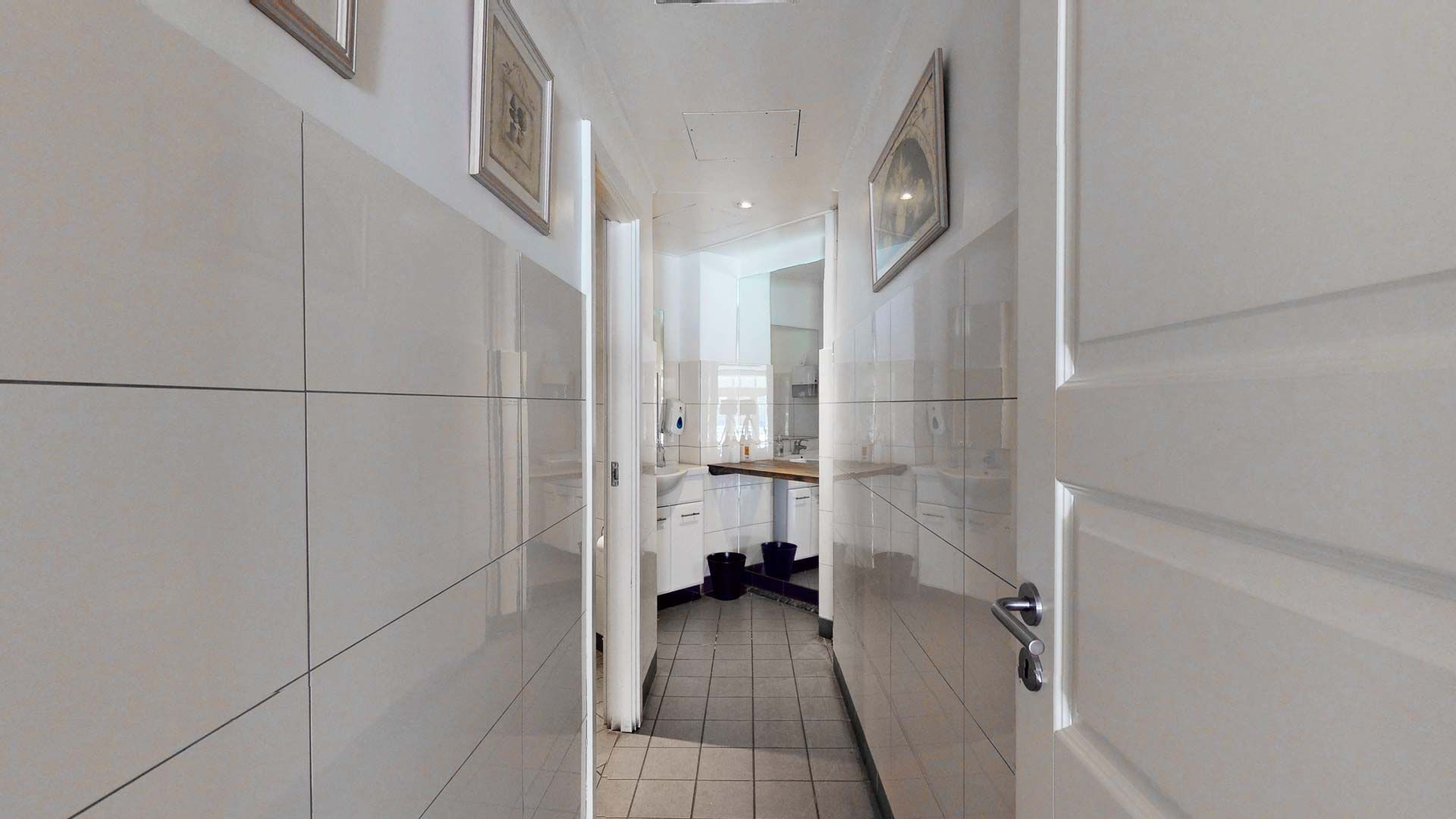 Foto af et toilet med hvide vægge, gulv og loft. Et spejl og to toiletter samt to hængebilleder på væggen