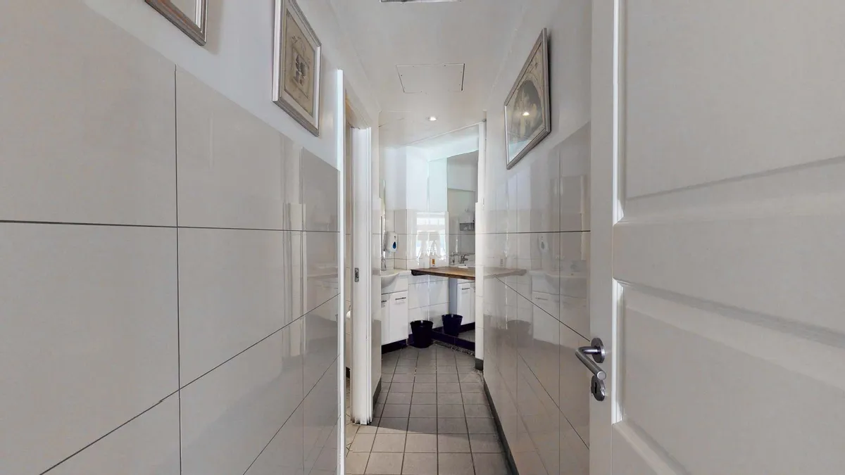 Foto af et toilet med hvide vægge, gulv og loft. Et spejl og to toiletter samt to hængebilleder på væggen