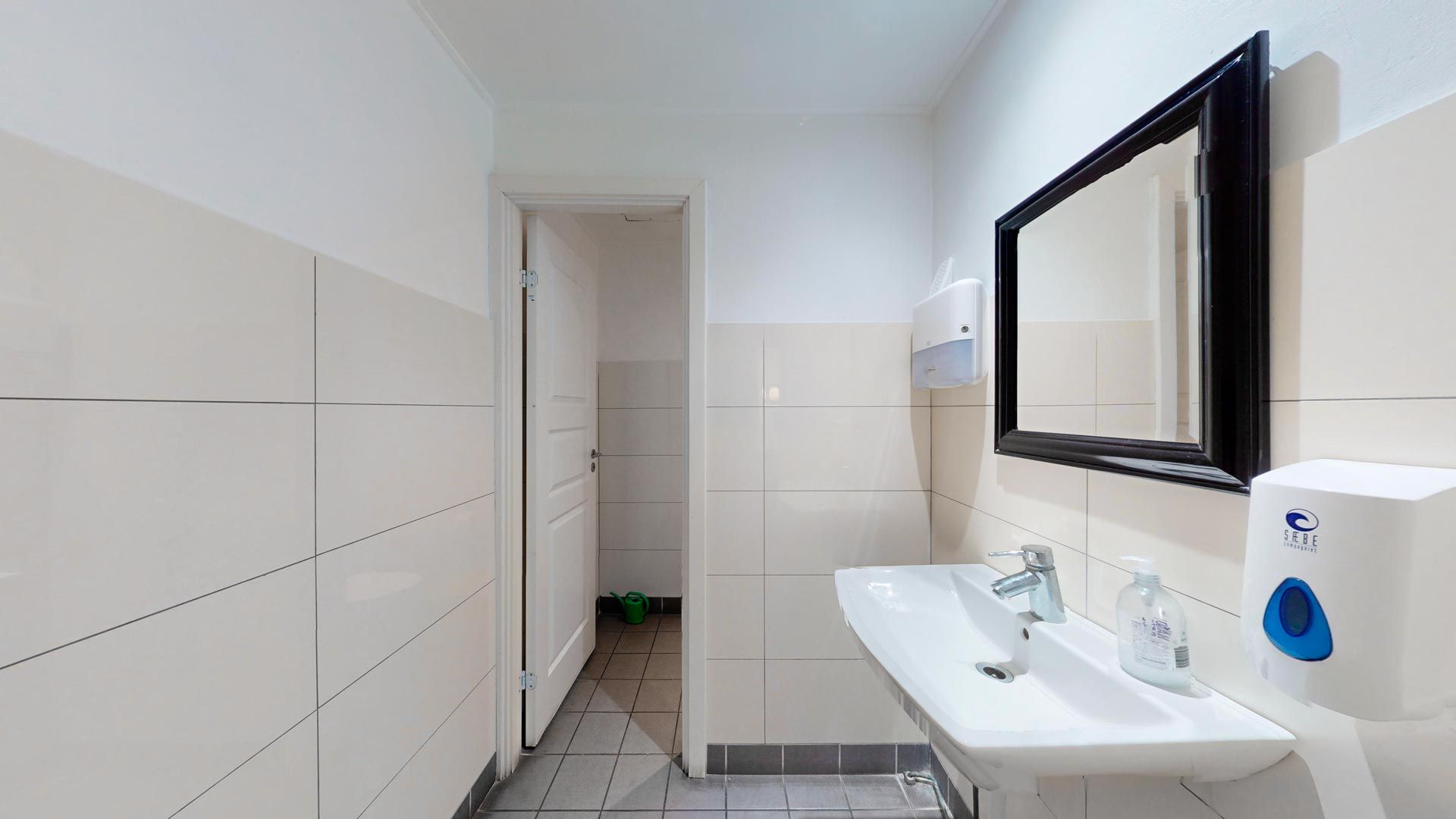 Rent, nyt toilet med hvidt tøjskab, hvidt badekar, sort spejl og to hvide håndsæber. En dør og en grøn vandkande udenfor.