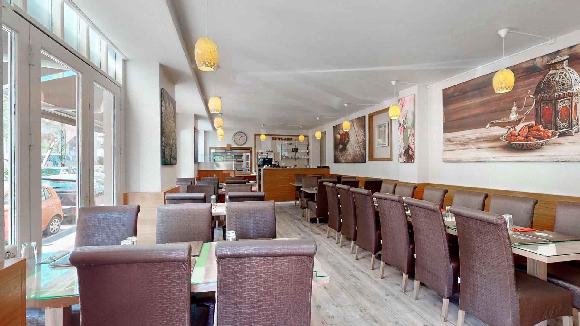 Lyst restaurant med grønne vægmalerier og bord og stole, smukt udstyret med lanterner og hængende lamper. Maleri på væggen med orientalsk lampeskærm og frugt.