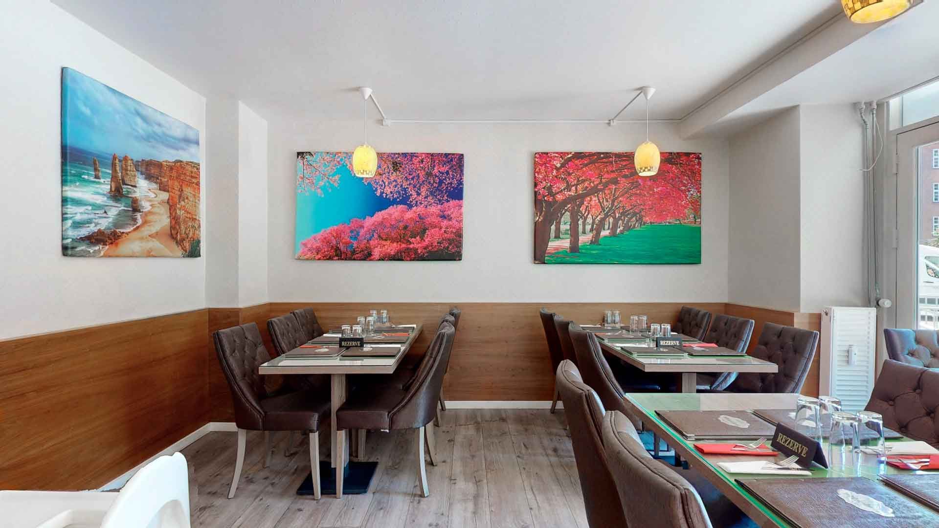 Indretningsmæssig restaurant med lyse møbler og malerier på væggene og lamper med lyse skjold over bordene