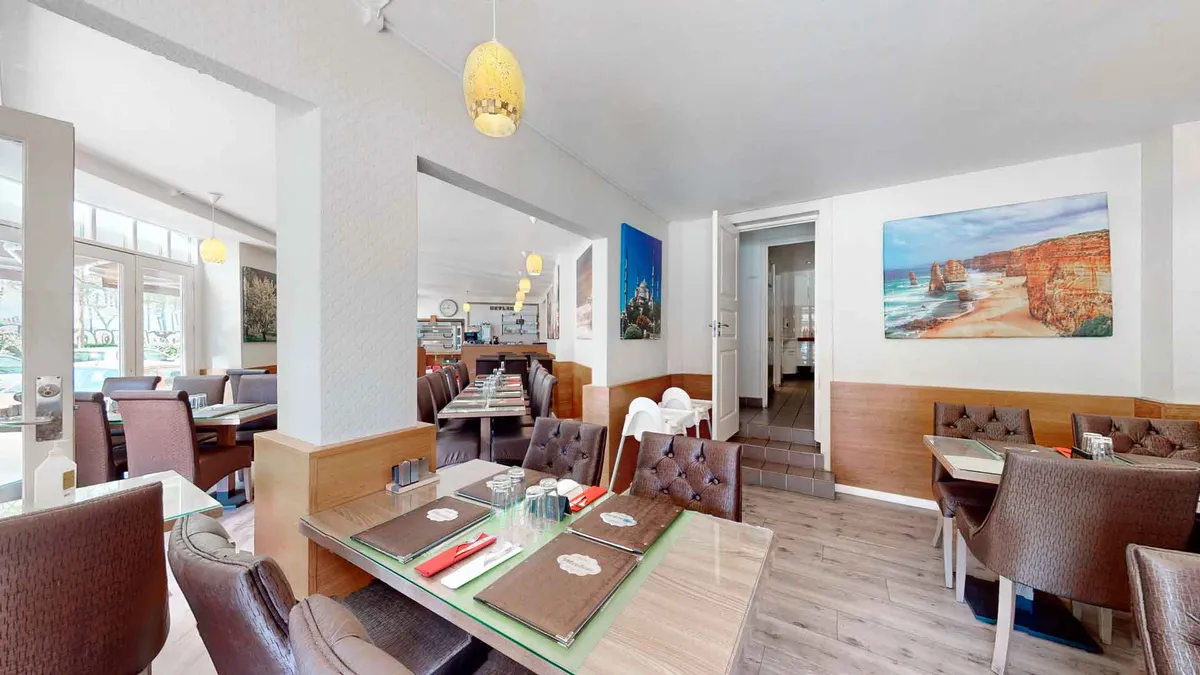 En restaurant med borde og stole, lysekroner, malerier og vinduer med udsigt til en have.