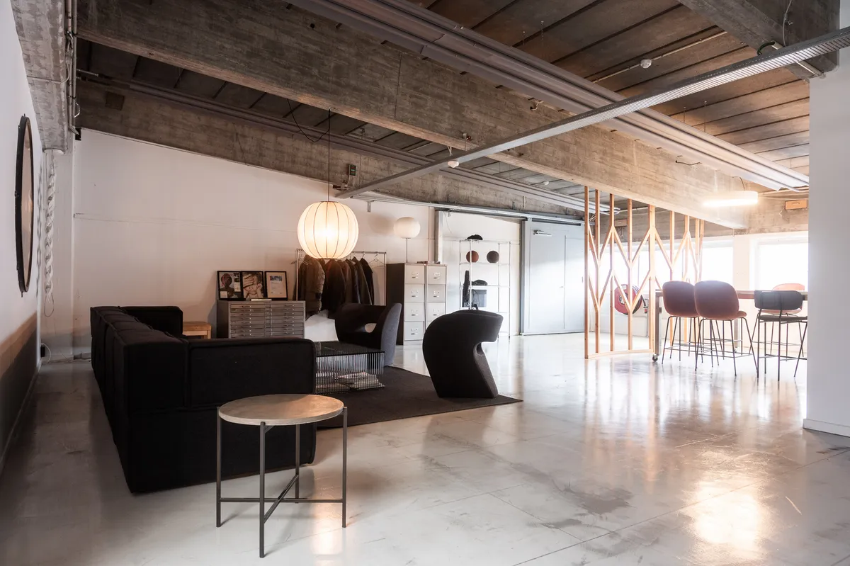 Kontor til leje på Raffinaderivej. Kontor med møbler og loftsbjælker i loftet. Værelse med sofa, stol, og højt gulv. Bord med plade og møbler til møder.