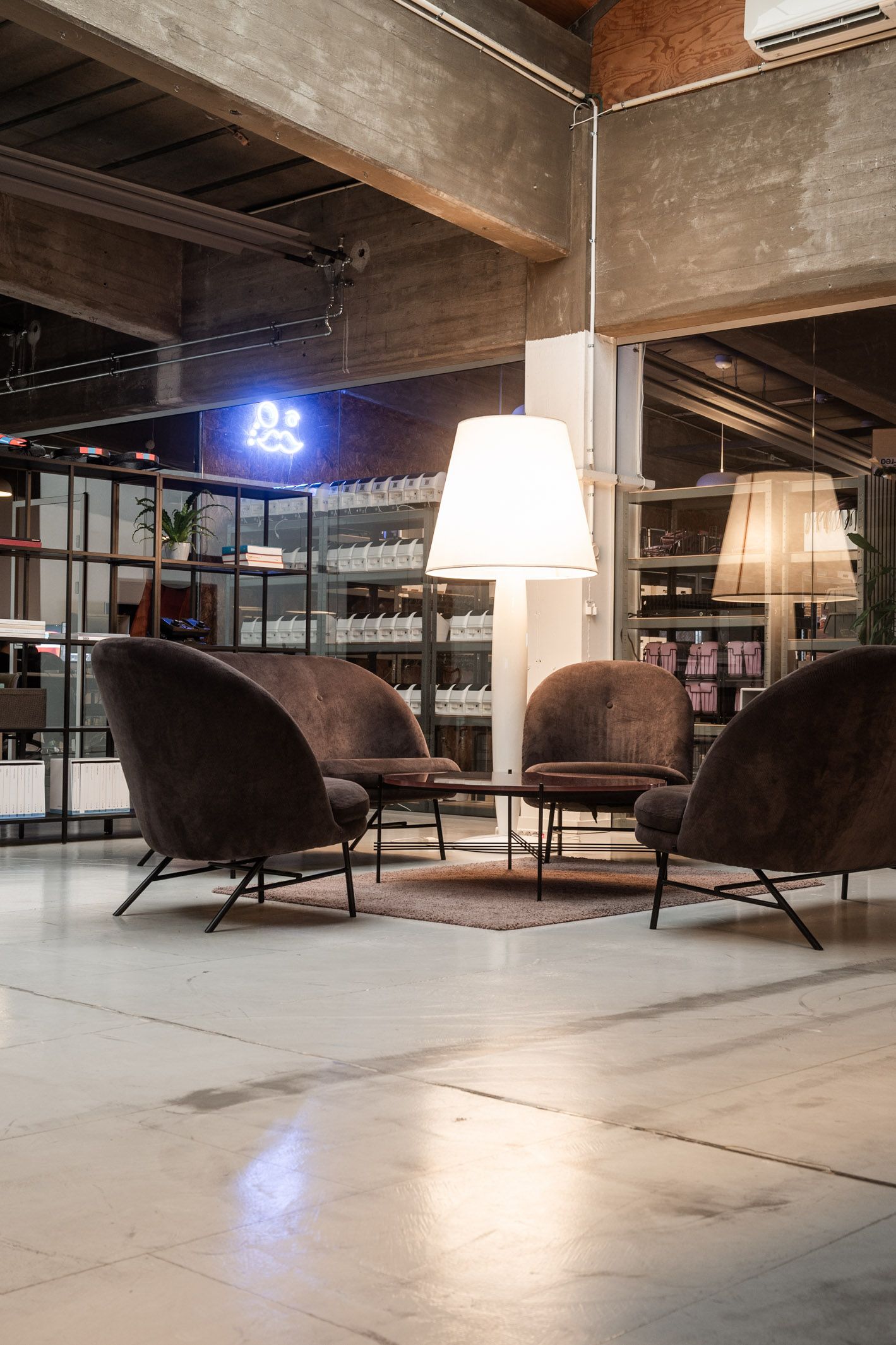 Moderne kontor med fire runde sofaer og to runde træborde under en stor hvid lampeskærm i loftet og lyserøde neonskilte