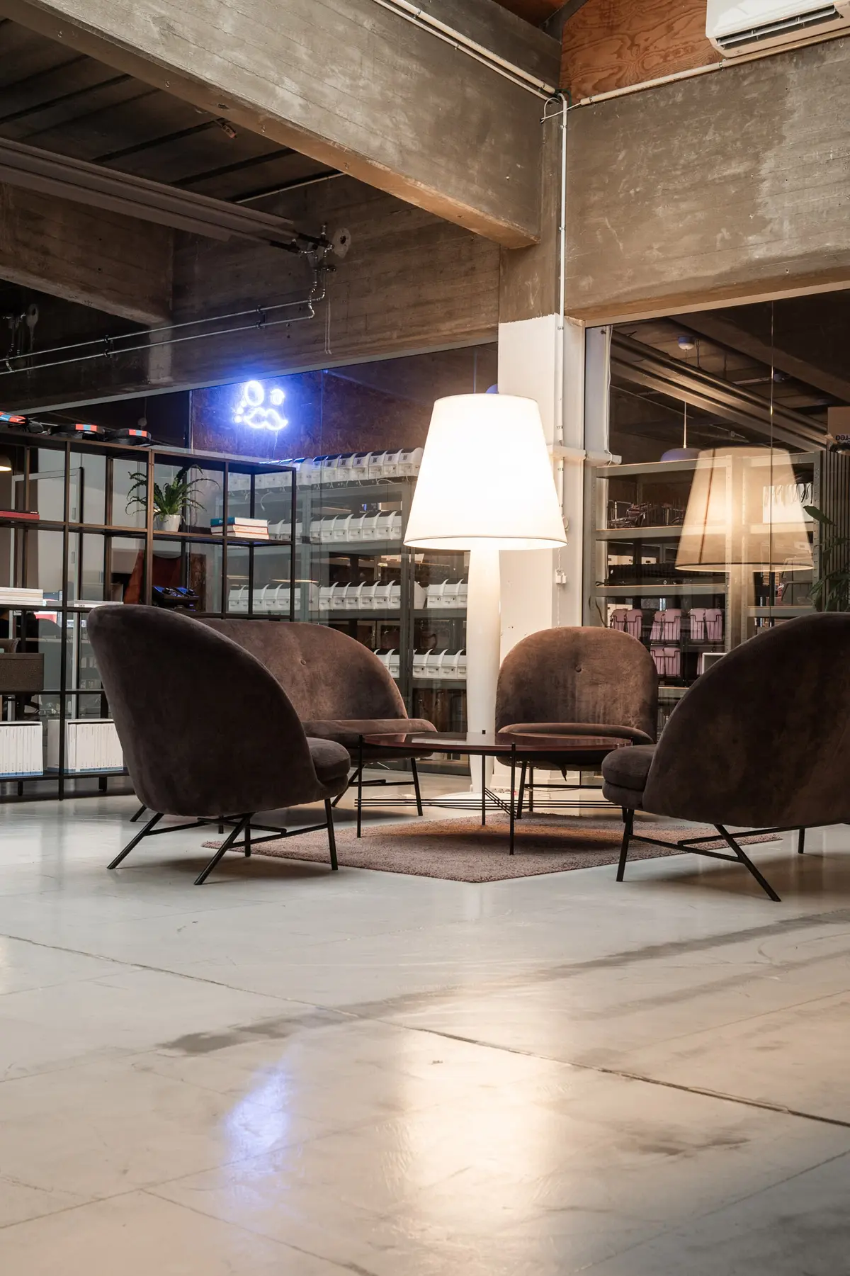 Moderne kontor med fire runde sofaer og to runde træborde under en stor hvid lampeskærm i loftet og lyserøde neonskilte