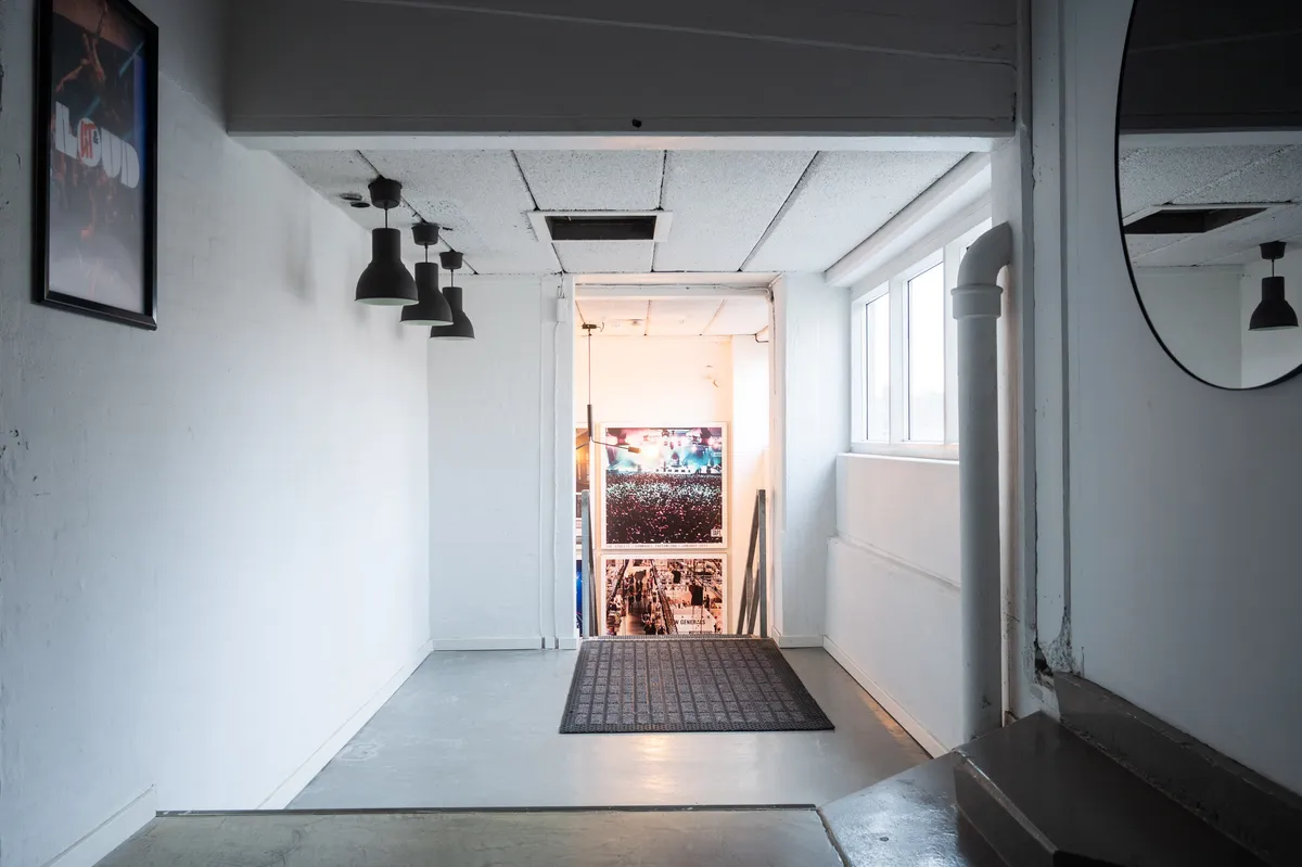 Københavns kontor med højt til loftet og lyse loftslampe i sort. Sort gulvtæppe foran døren og spejl med lyserefleks. Plakat med tekst og billede og en indgang til en anden lokal