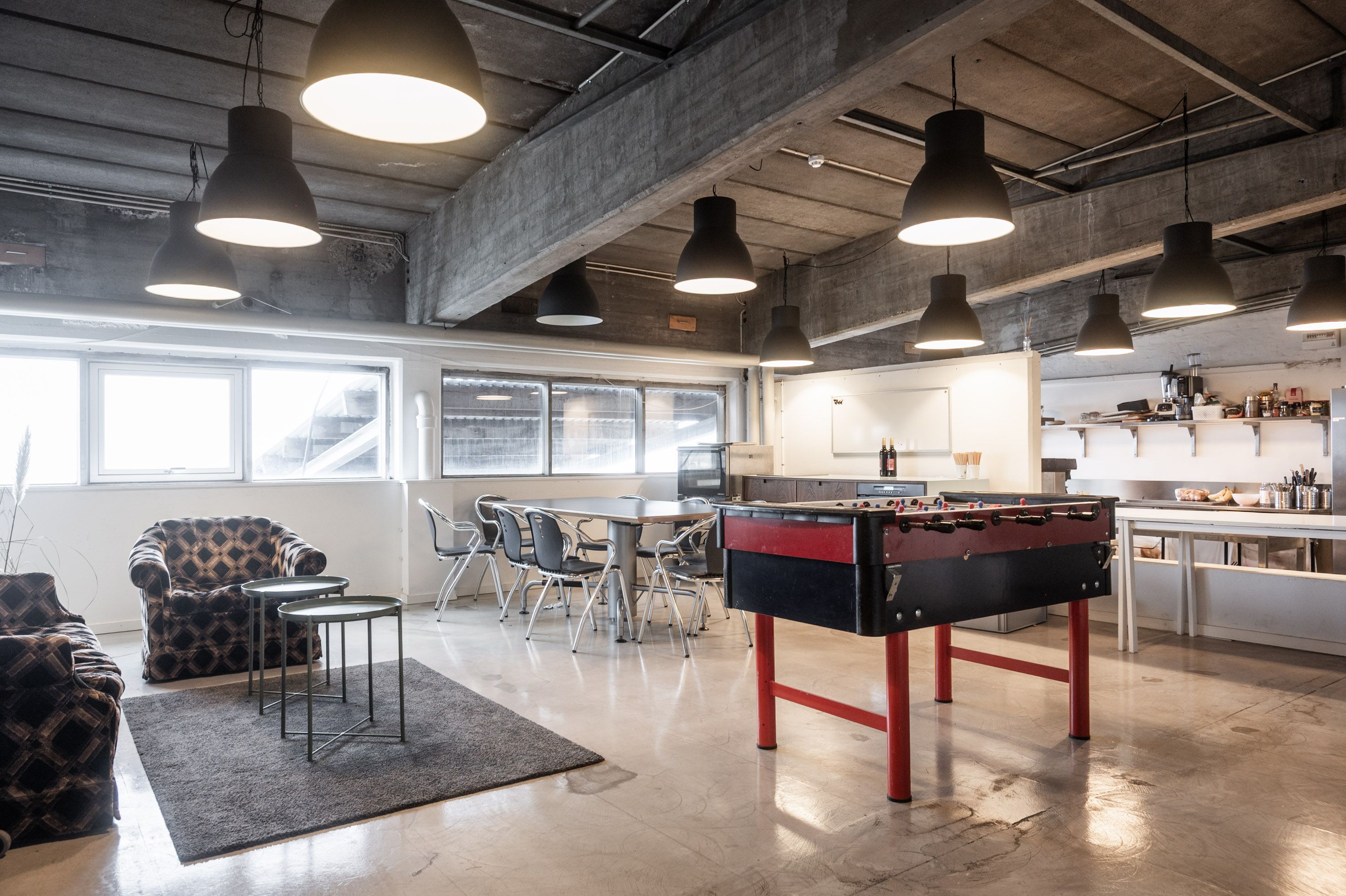 Rå og karakterfuldt kontor med bord og fodboldbord på Raffinaderivej i København S med køkken med mange hylder og vinflasker