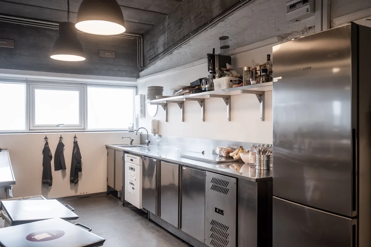 Råt kontor med lyse loftslampe, to vasker og køleskab i industrikvarter på Amager i København S. Kontor med lyseruder og loftslampe i industrikvarter.