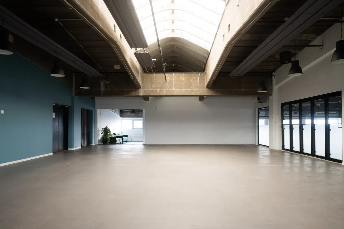 Kontor til leje i Råt og karakterfuldt kontor i de ikoniske spritfabrikker på Amager, midt i TAP 1 på Raffinaderivej. Moderne loft med lyseglas og hængelampe. Hvid og blå væg, og glasdøre og vinduer