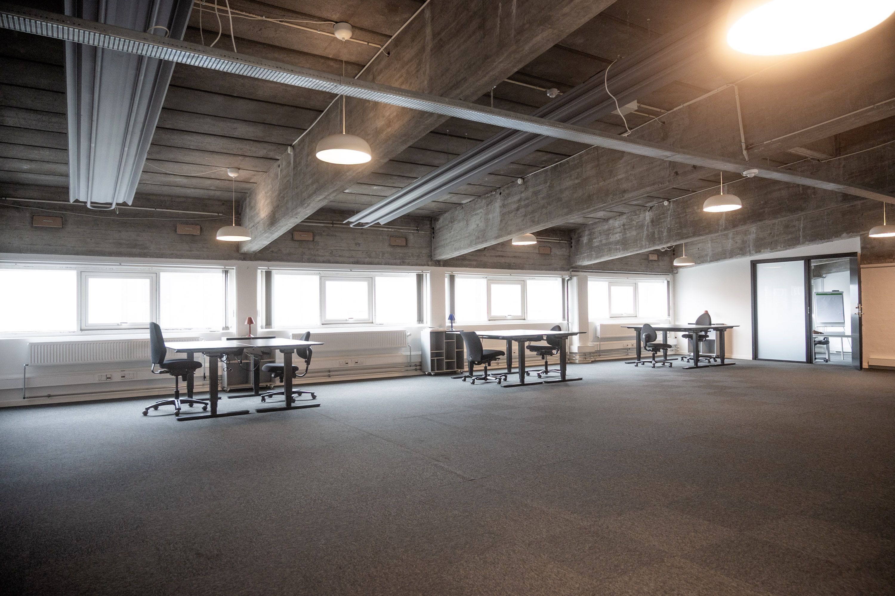 Kontor med lyse lofter og gulvbelægning samt møbler, der er arrangeret rundt om bordene