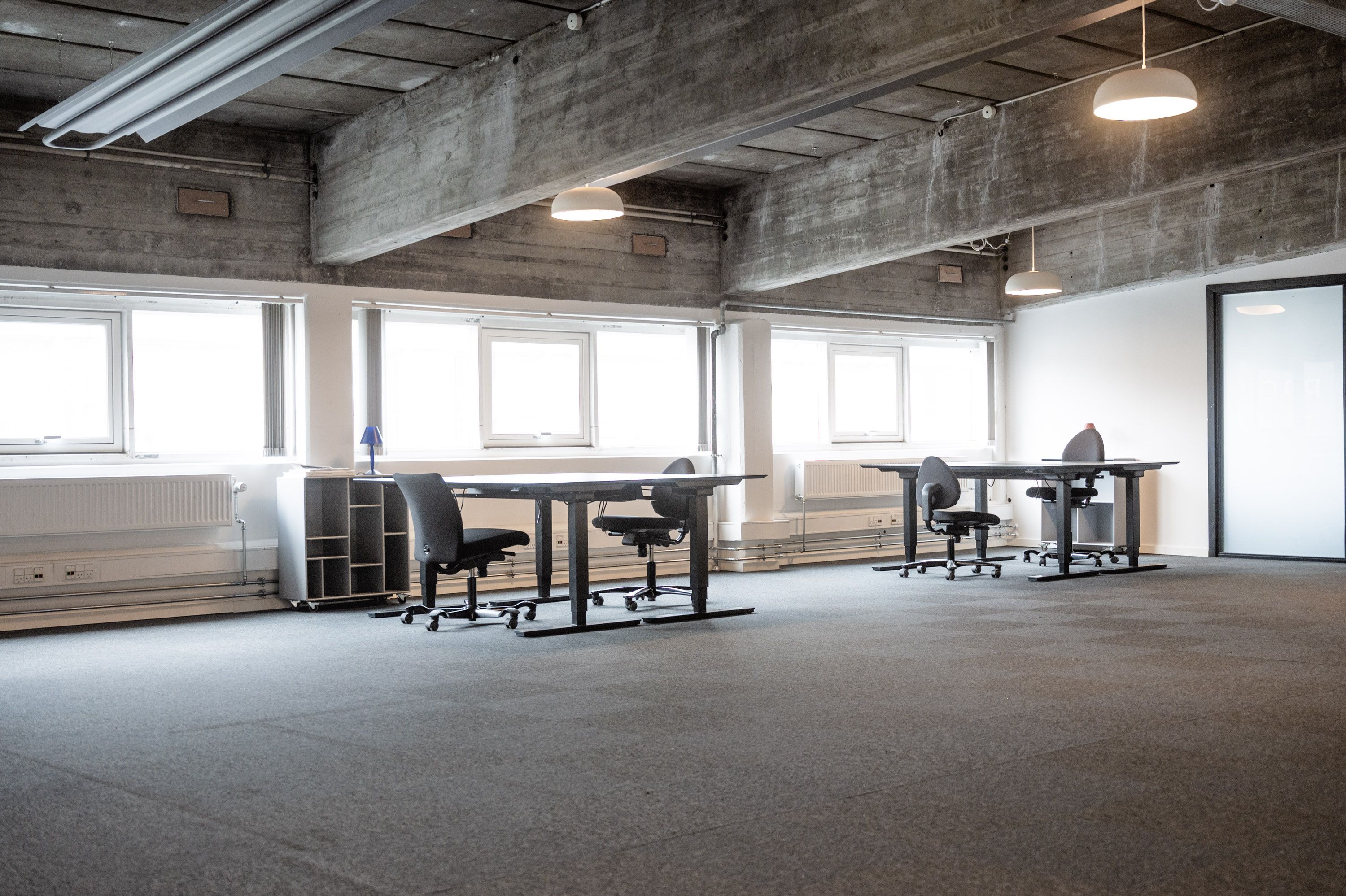 Kontor til leje med store vinduer og lyse lofter. Værelser med skriveborde og stole. Moderne design med lysekroner og højt loft