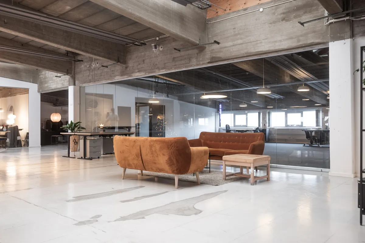 Rå og storslået kontor med lyse lofter, glasvægge og lysekroner med gule lamper i københavnsk industriindretning