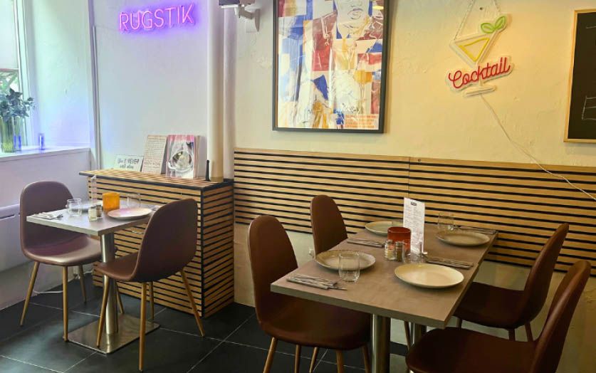 Indenfor en hyggelig café med lyse neonskilte og moderne interiør, hvor borde og stole er sammensat med omsorg og smag