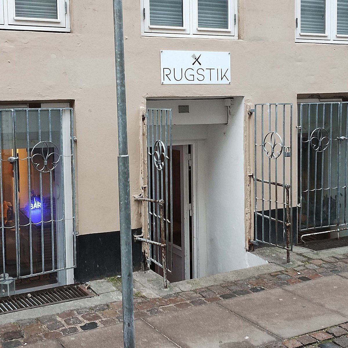Rustne metaldøre med låse og udsigt til café med 3 Bar-skilt, placeret på en stenbrolægget gågade i København