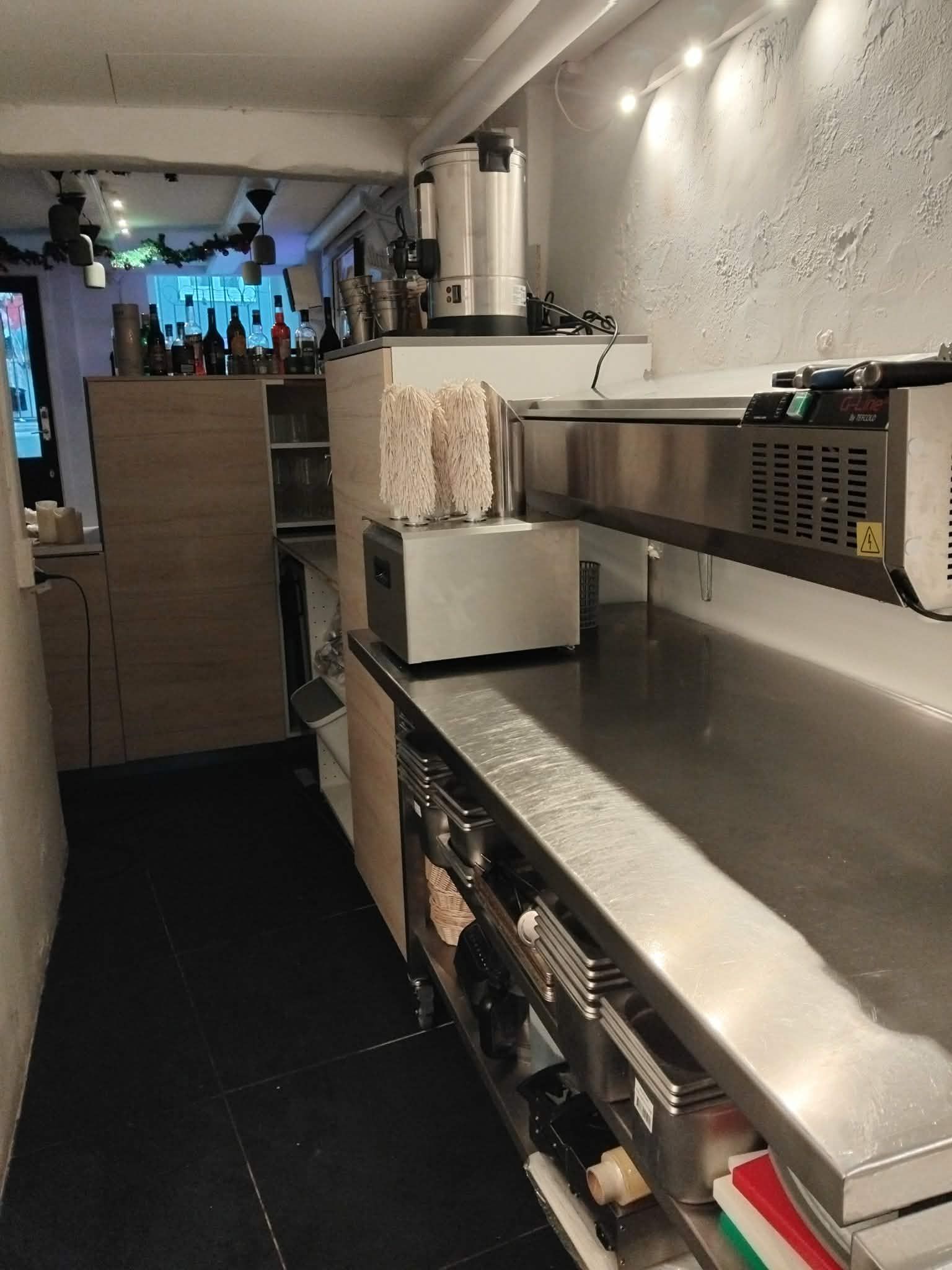 Køkken med flere apparater, en stor maskine og et loft med flere lamper og en udsigt til en butiksfront med vinduer og døre