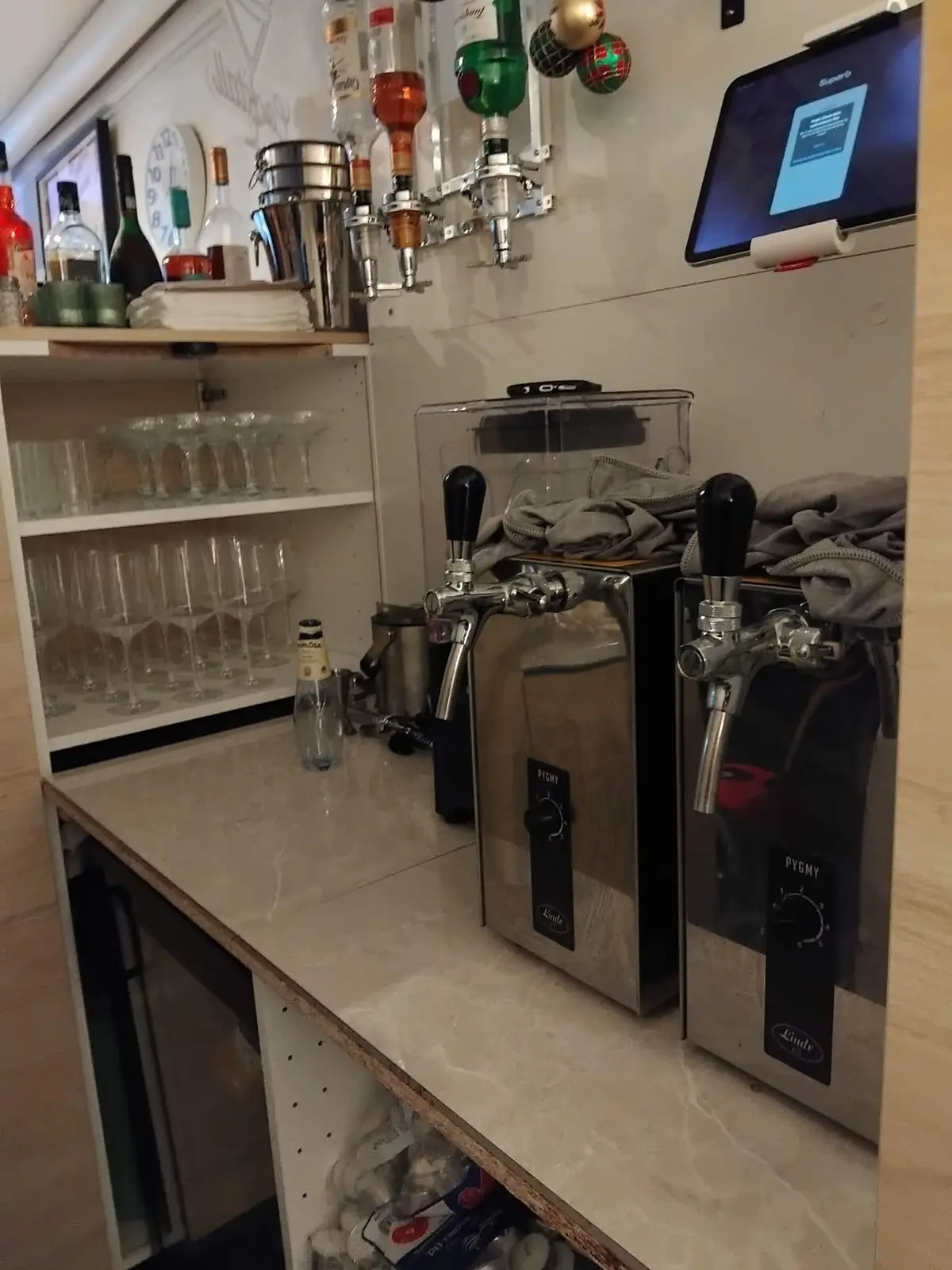 Cafe med bar, øltapper, glas og flasker samt monitor på væggen og en tidsviser