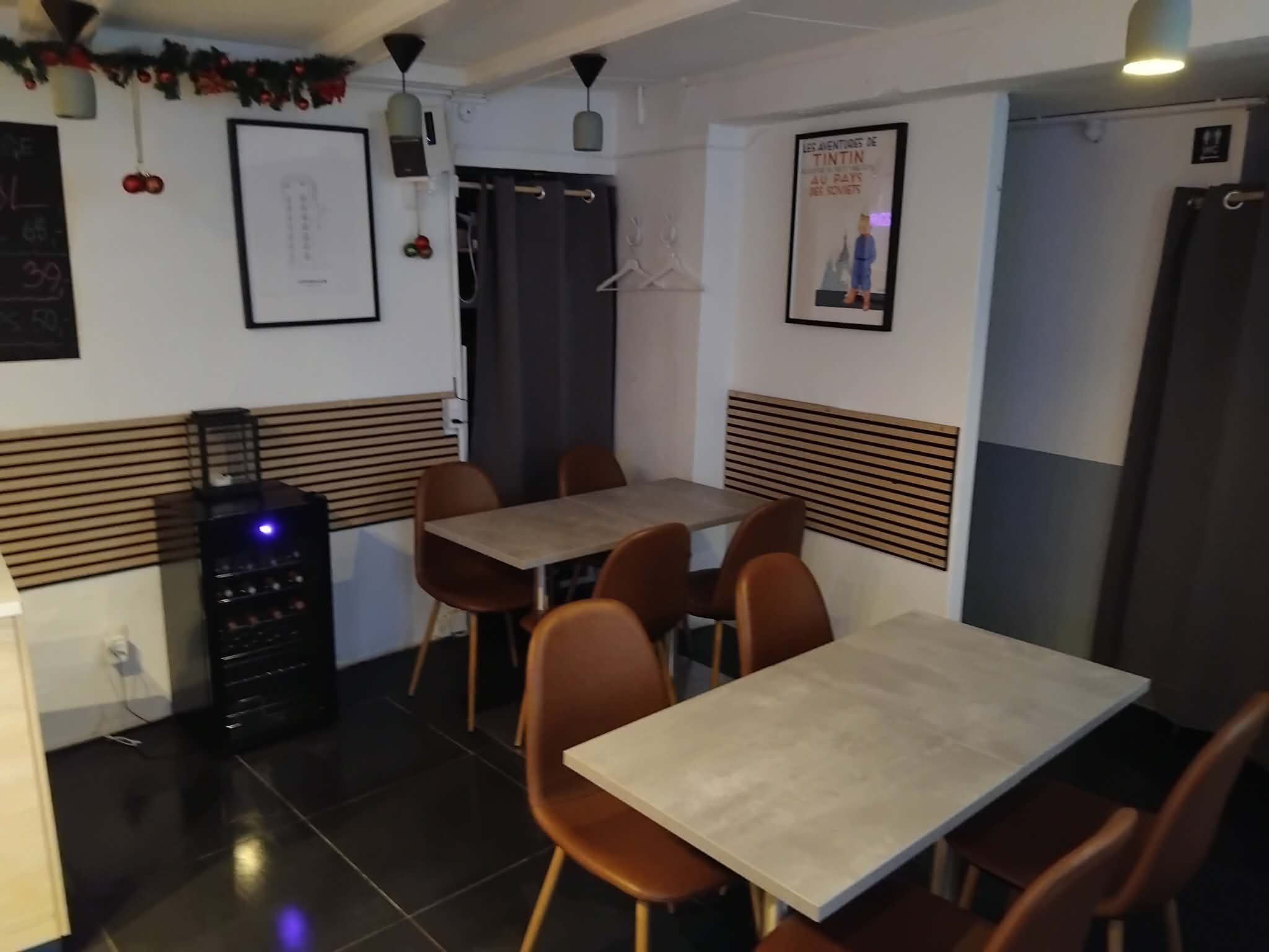 En hyggelig café med møbler og spisesteder med borde og stole samt en køleskab med drikkevarer og en væg med skrift og billeder samt en skorsten i loftet