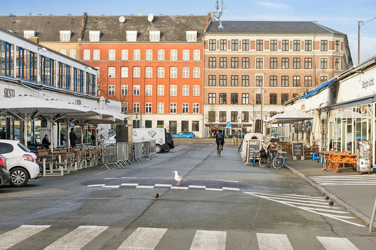 Kontorlejemål med terrasse og udsigt over byen i København, med restauranter og mennesker i forgrunden, og en cykel i baggrunden.