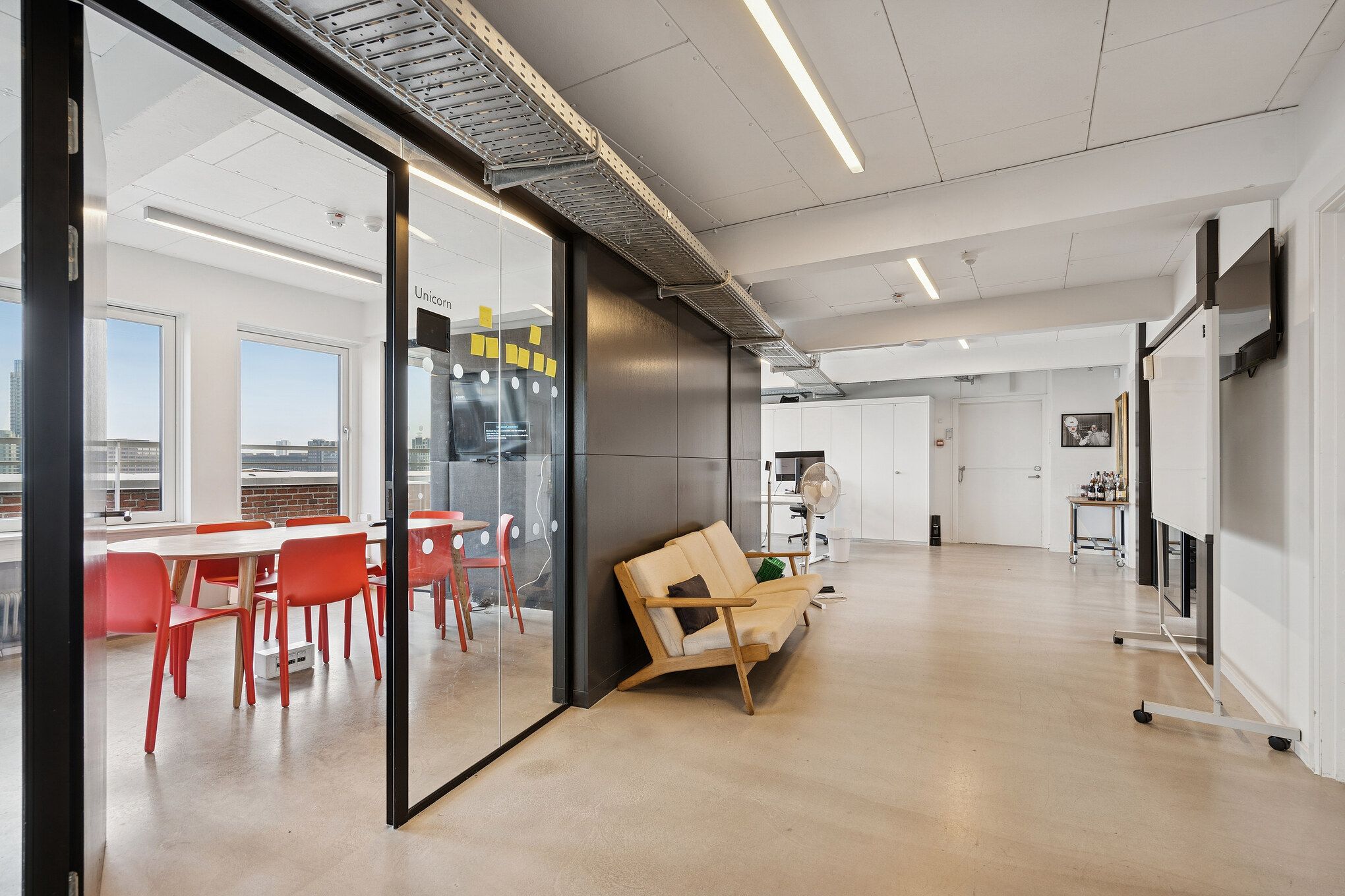 Moderne kontor med hvid gulv og møbler samt udsigt over byen, hvor der er en rund bord med røde stole og en sofa med pude