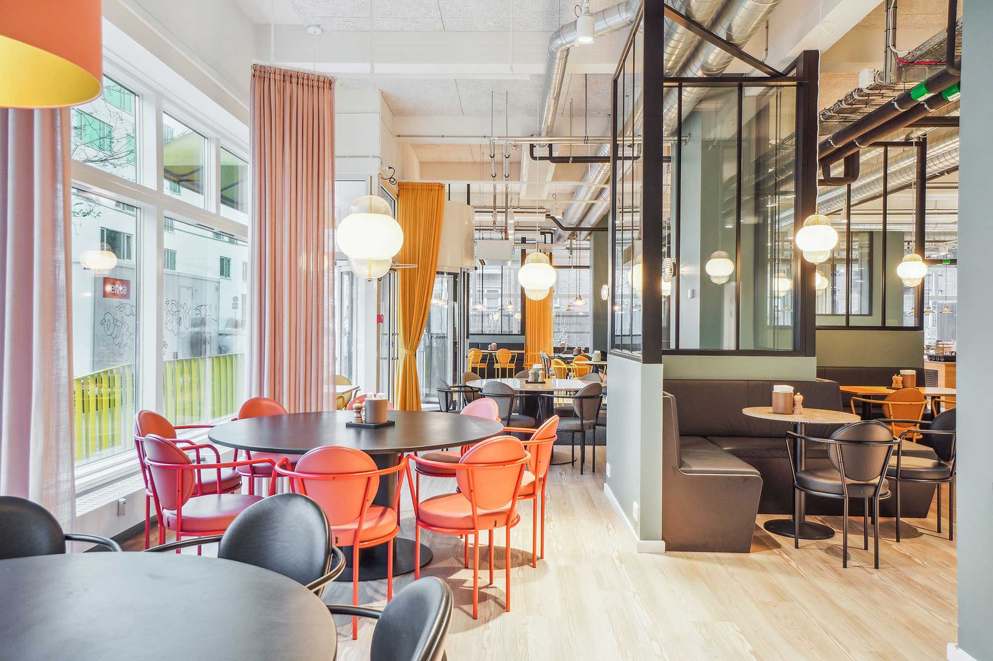 Kontor med runde borde og lyserøde stole, der vender mod store vinduer med byudsigt, møbler og loftslampe lyser varmt og lyserødt