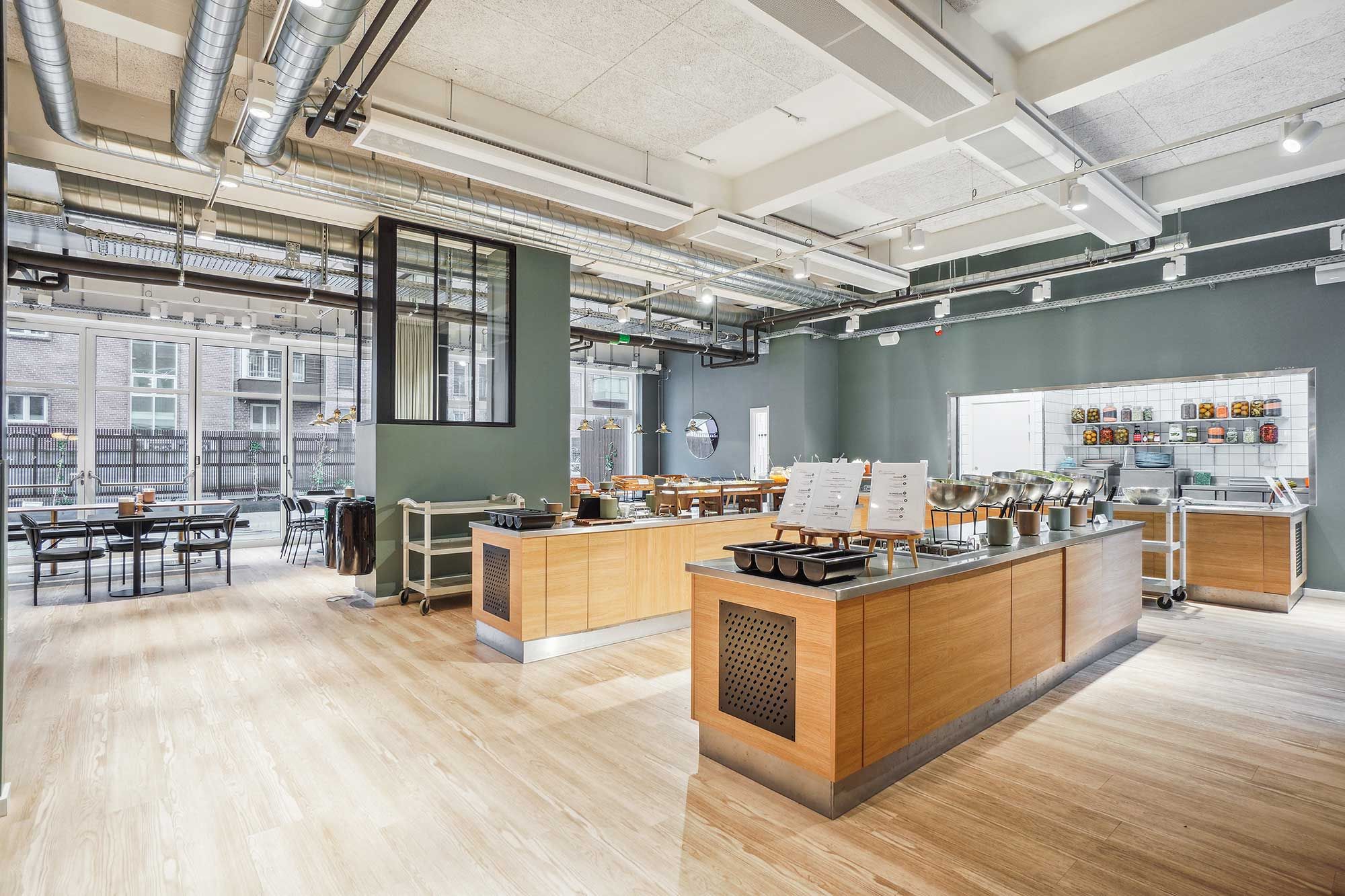 Kontor med højt til loftet og lyse loftsvinduer, hvid loftsbjælke og møbler med grønne vægge, trægulve og bord og stole samt terrasse med udsigt over byen