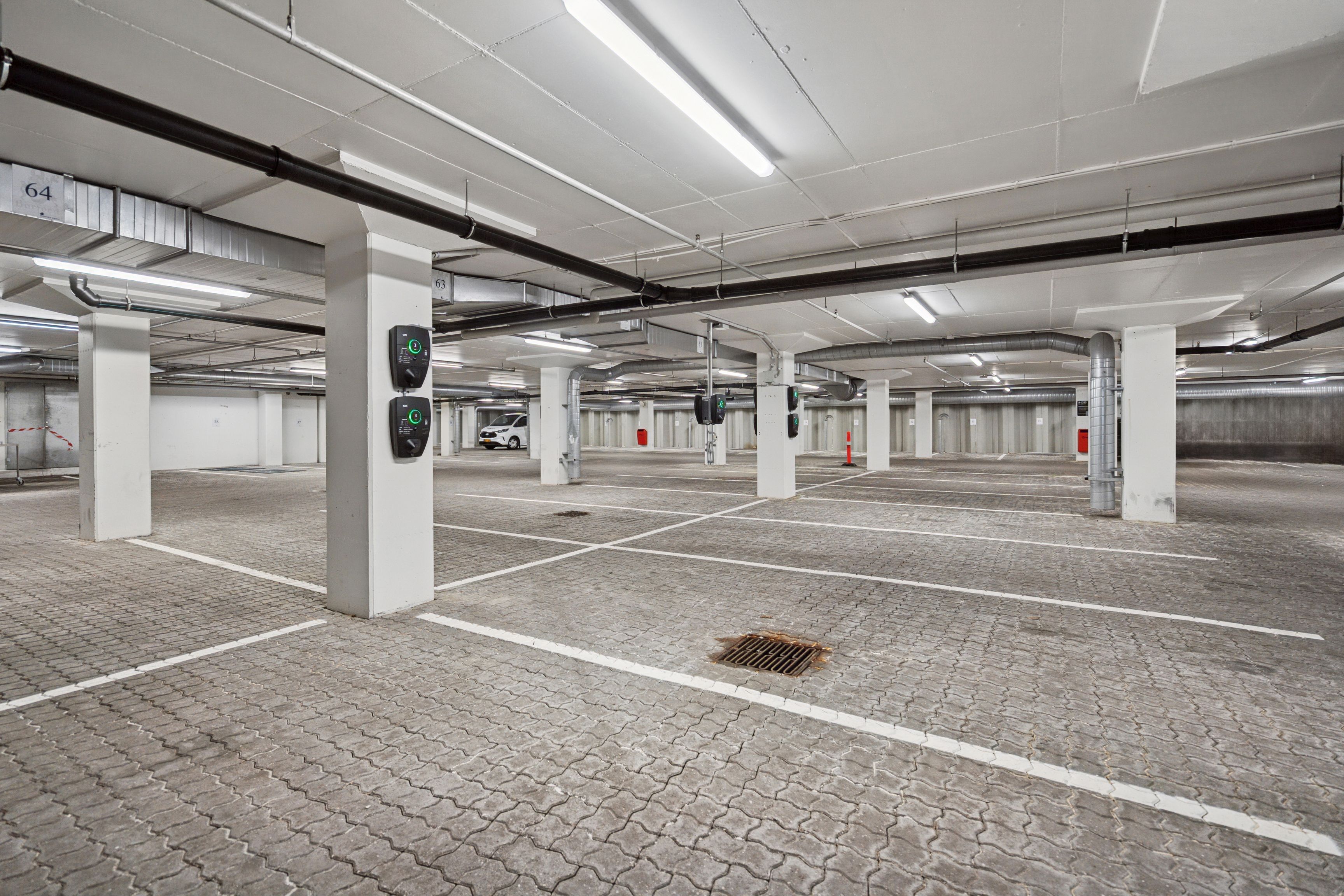 Stort og lyst underjordisk parkeringsplads med højt til loftet og hvide søjler samt flere parkeringsautomater og en bil i baggrunden