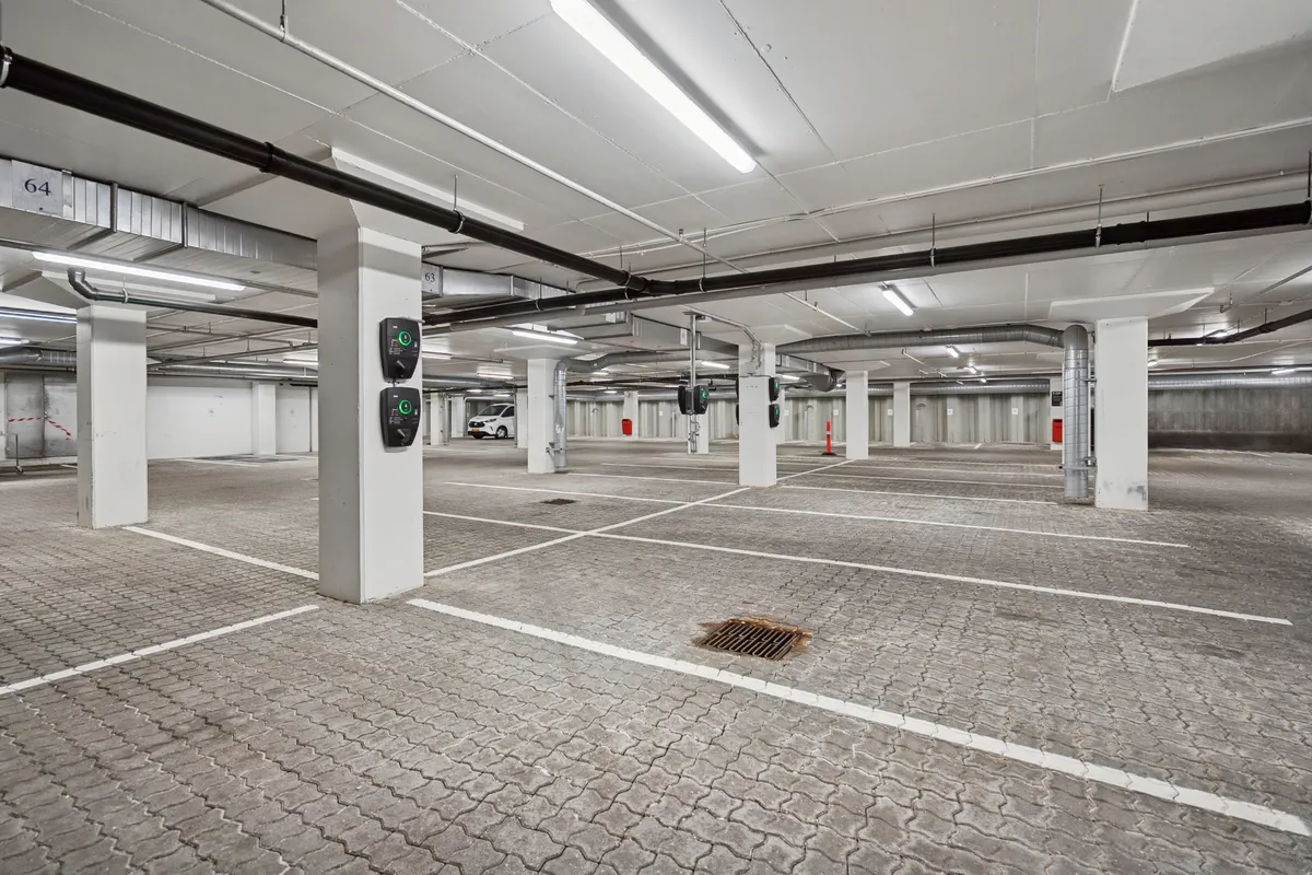 Stort og lyst underjordisk parkeringsplads med højt til loftet og hvide søjler samt flere parkeringsautomater og en bil i baggrunden