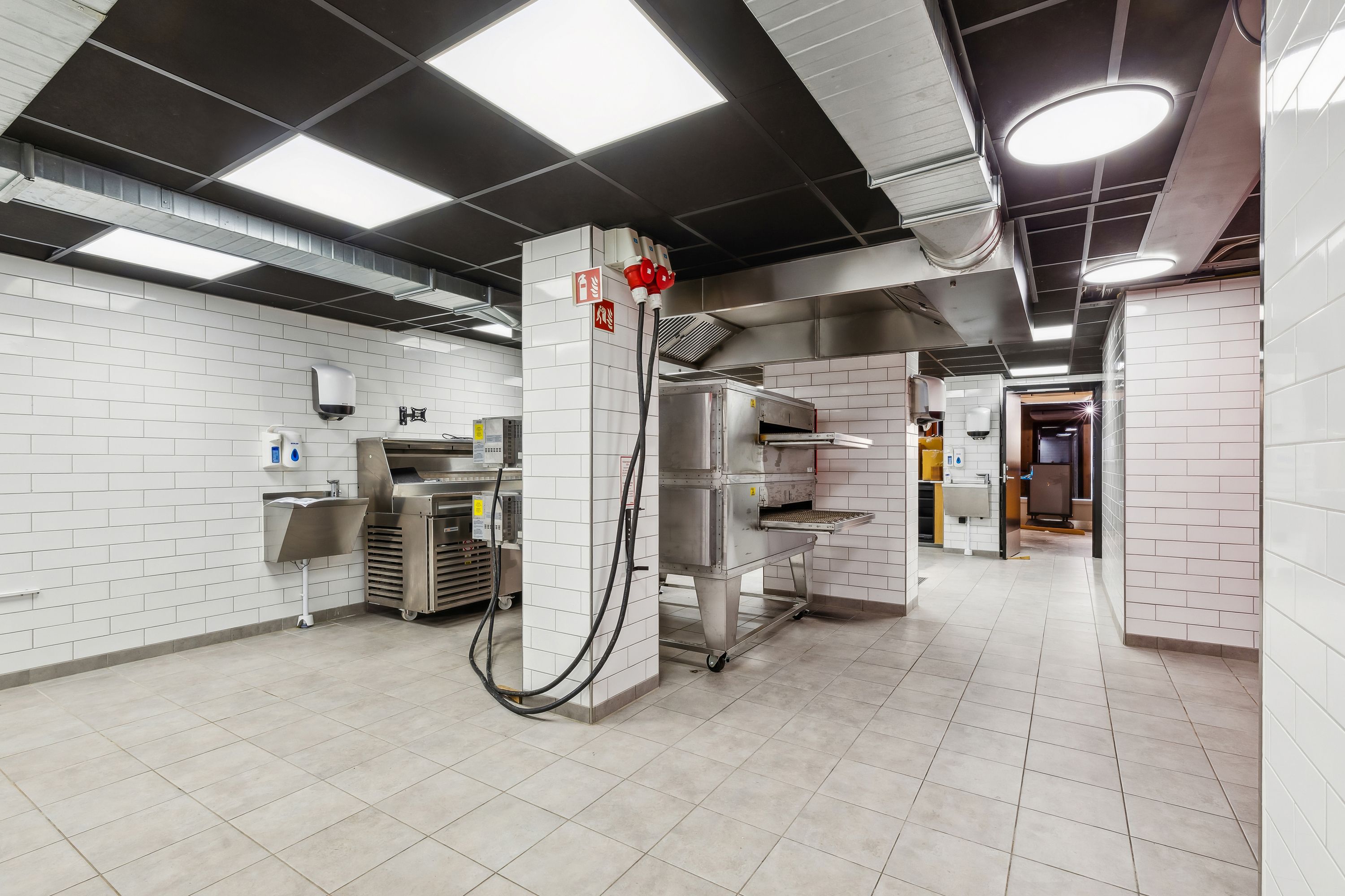 Take-away i lejemål med højt til loftet, hvid tøjle og lysegule vægge. Der er moderne ovne og en håndvask til forberedelse.