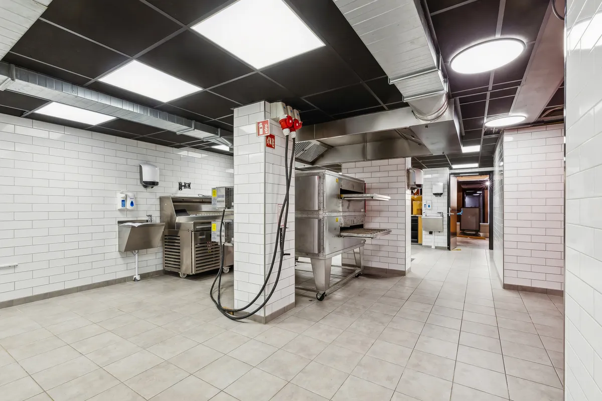 Take-away i lejemål med højt til loftet, hvid tøjle og lysegule vægge. Der er moderne ovne og en håndvask til forberedelse.