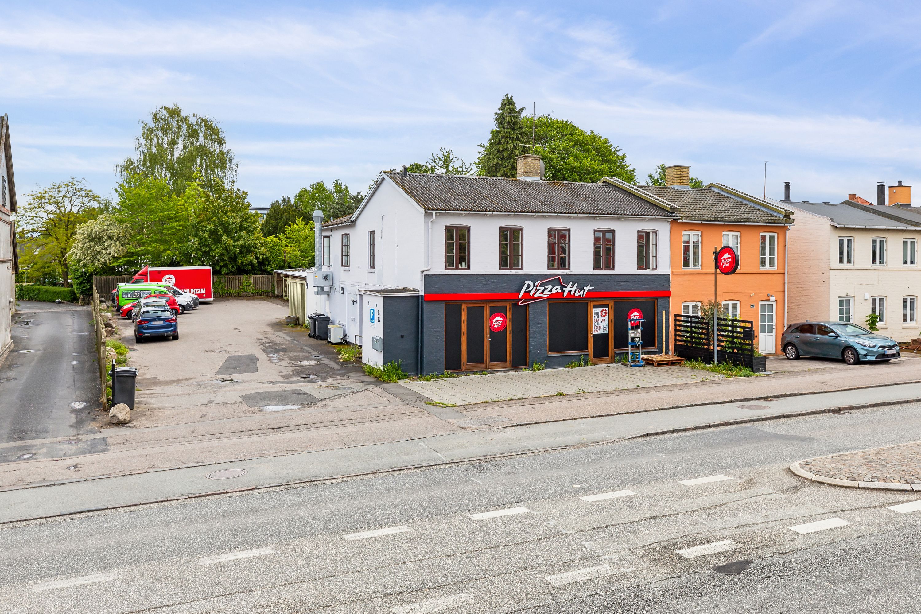 Pizzaria med take-away er lejet og har parkeringsplads med biler parkeret foran og en Pizza Hut-vogn står parkeret i baggrunden