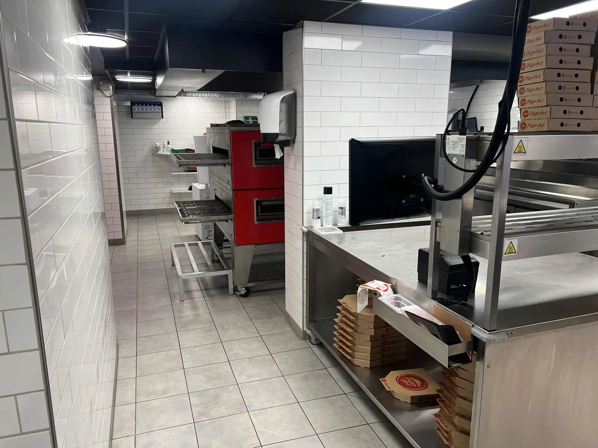 Take-away med røde ovne og køkkenudstyr, der udsender en professionel atmosfære. Væggene er hvide og udstyret med moderne belysning.